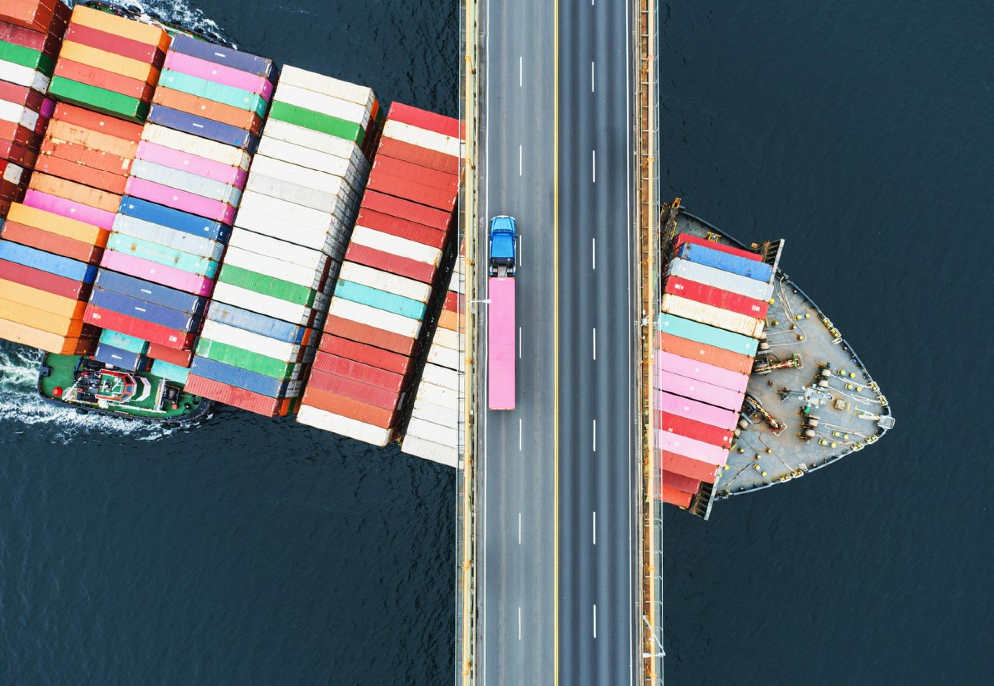 Big freight ship passing under a road bridge with a truck on it