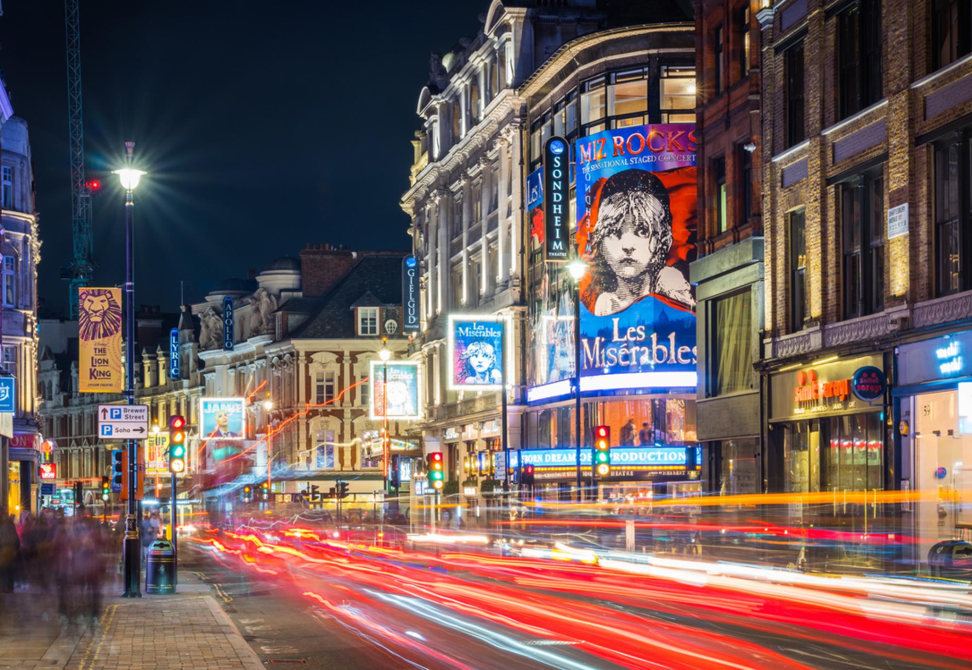 Traffic zooming along Shaftesbury Avenue past the tourist crowds and the billboards of London’s vibrant theatre district at night.