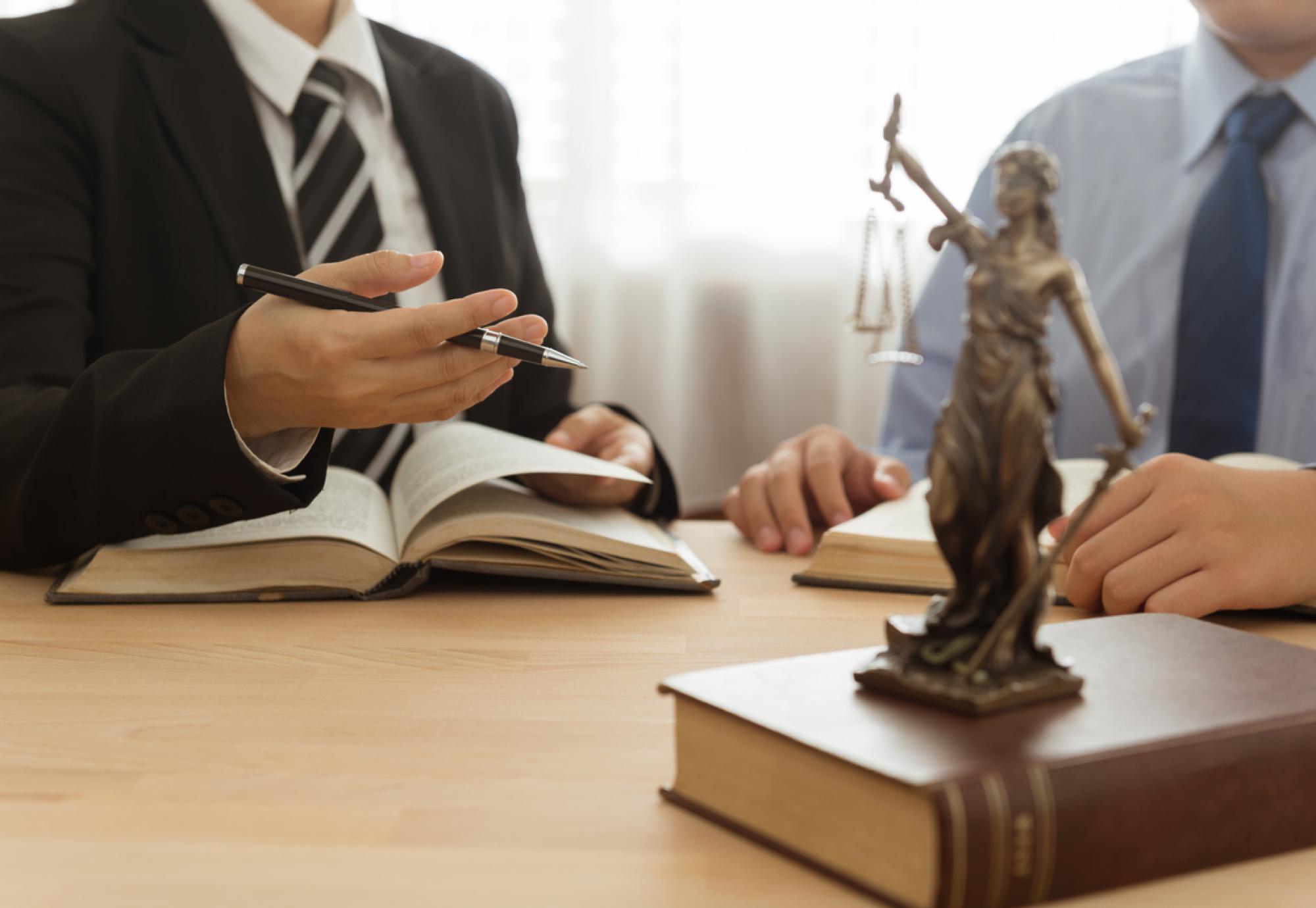 Two lawyers working, justice statue sits in the foreground on the table