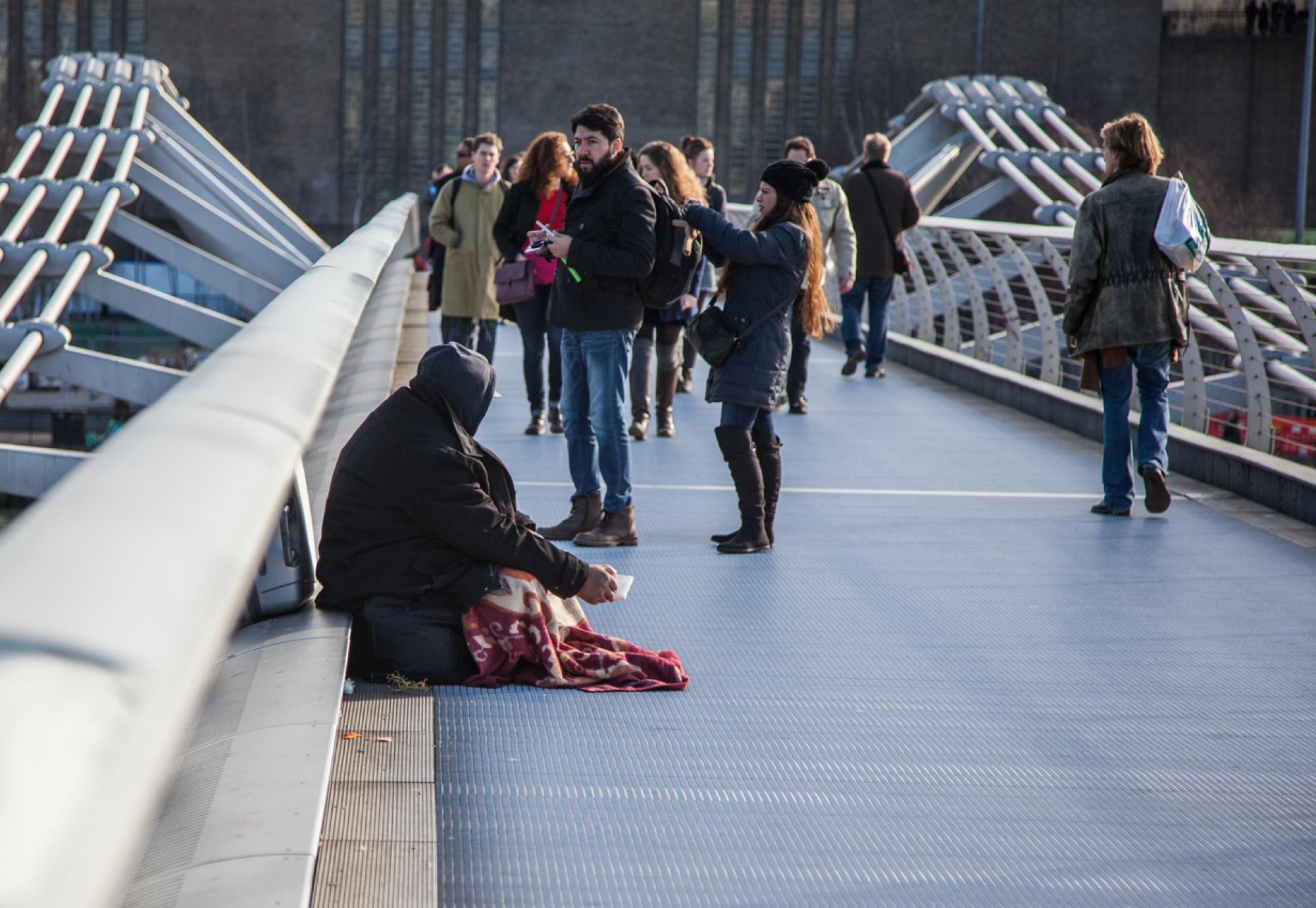 Homeless person surrounded by tourists on a bridge in London