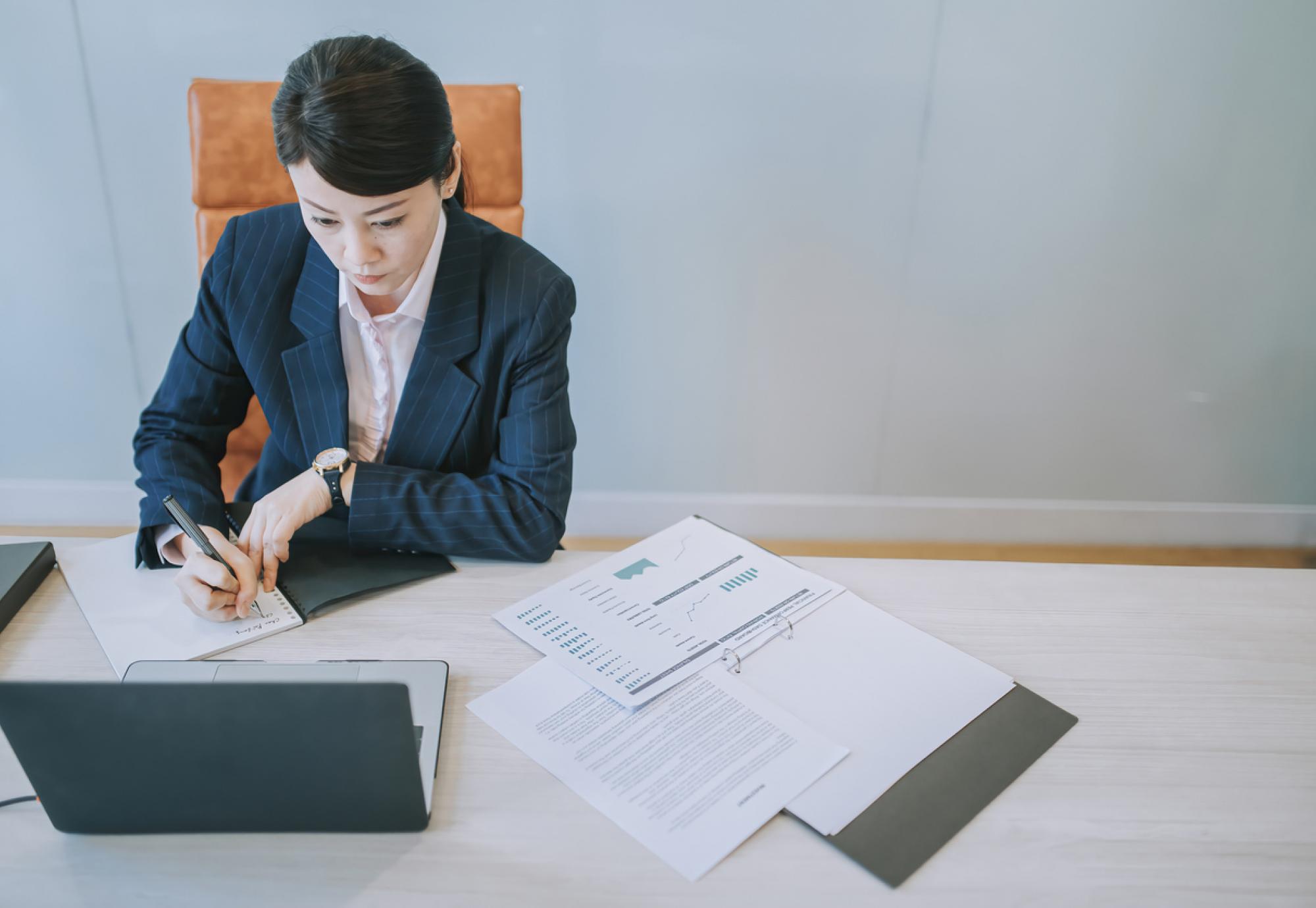 Woman working on a laptop with papers on the desk in front of her