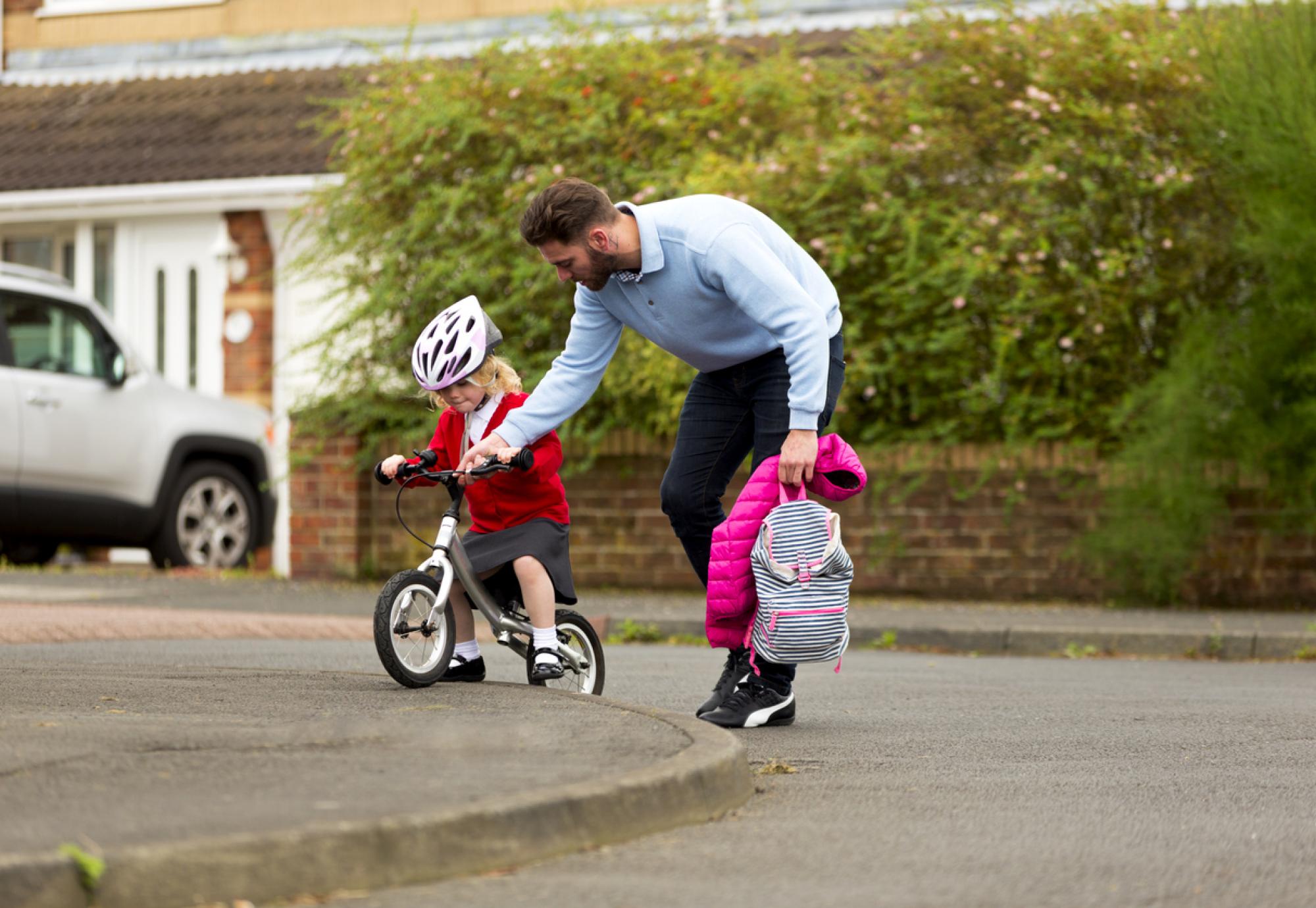 Dad helping his daugher cycle to school