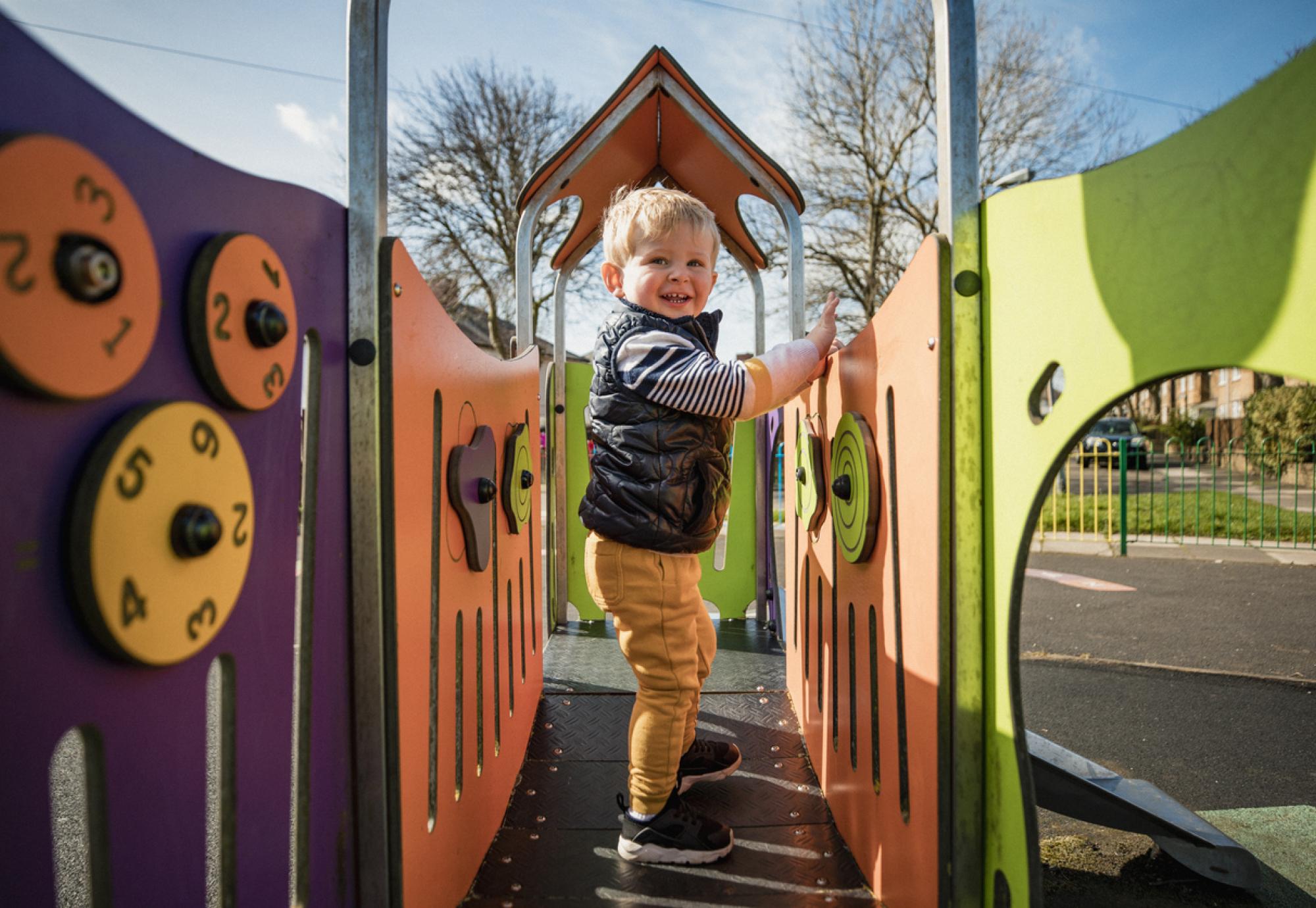 Young boy playing at a public park on a climbing frame on a sunny day
