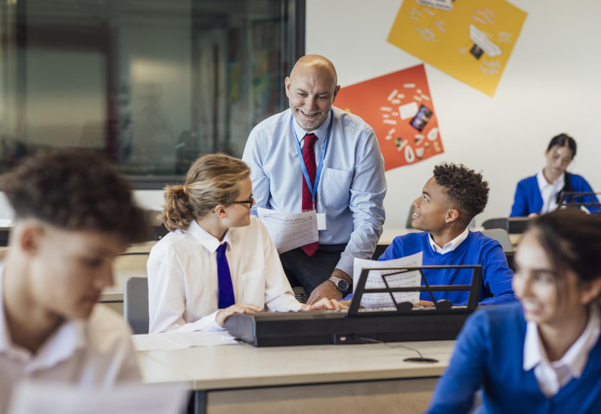 front-view shot of teenage music students in a classroom learning how to play the keyboard with their teacher at a school