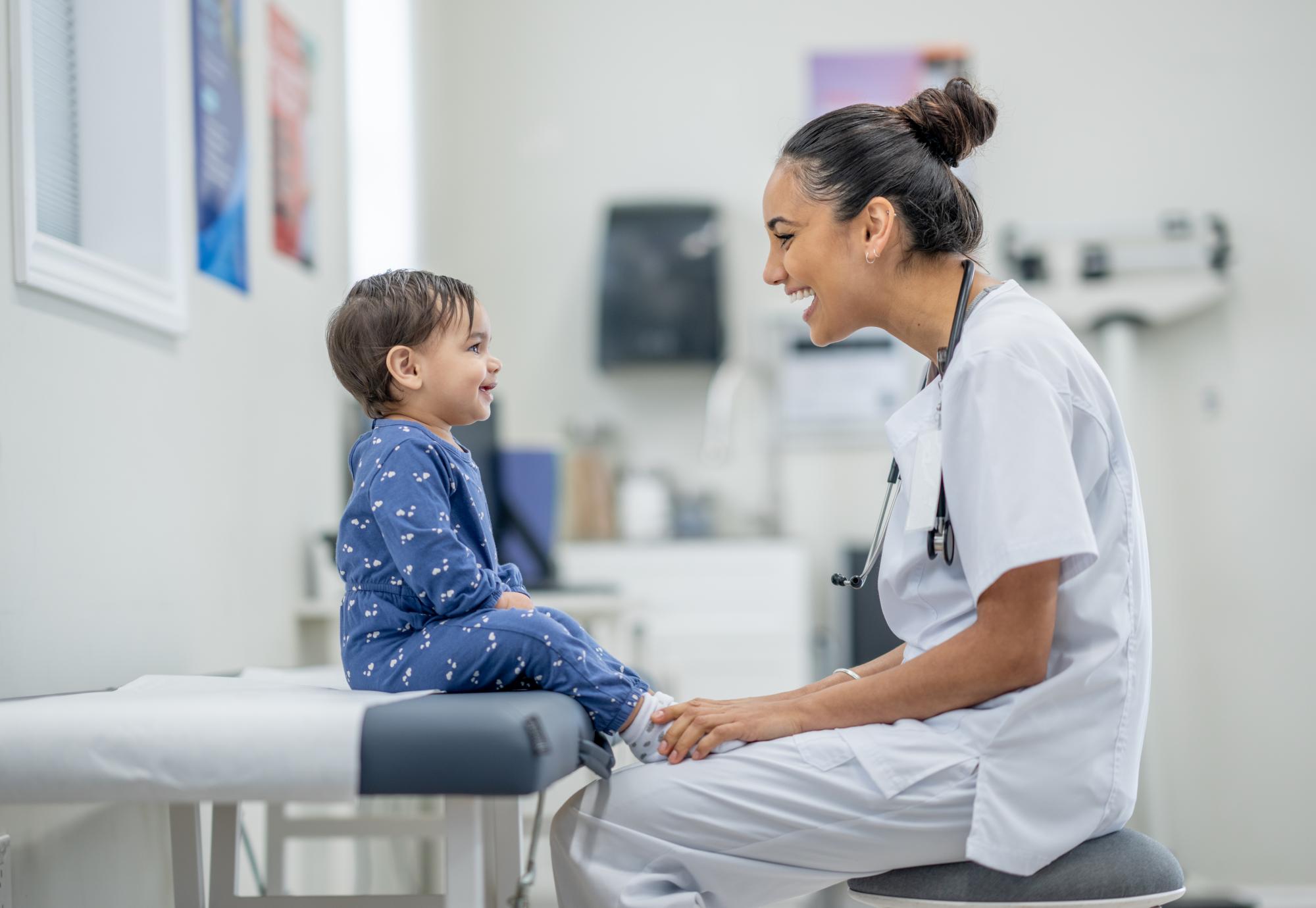 A sweet little toddler sits up on an exam table in a doctors office as her female doctor conducts a routine check-up.