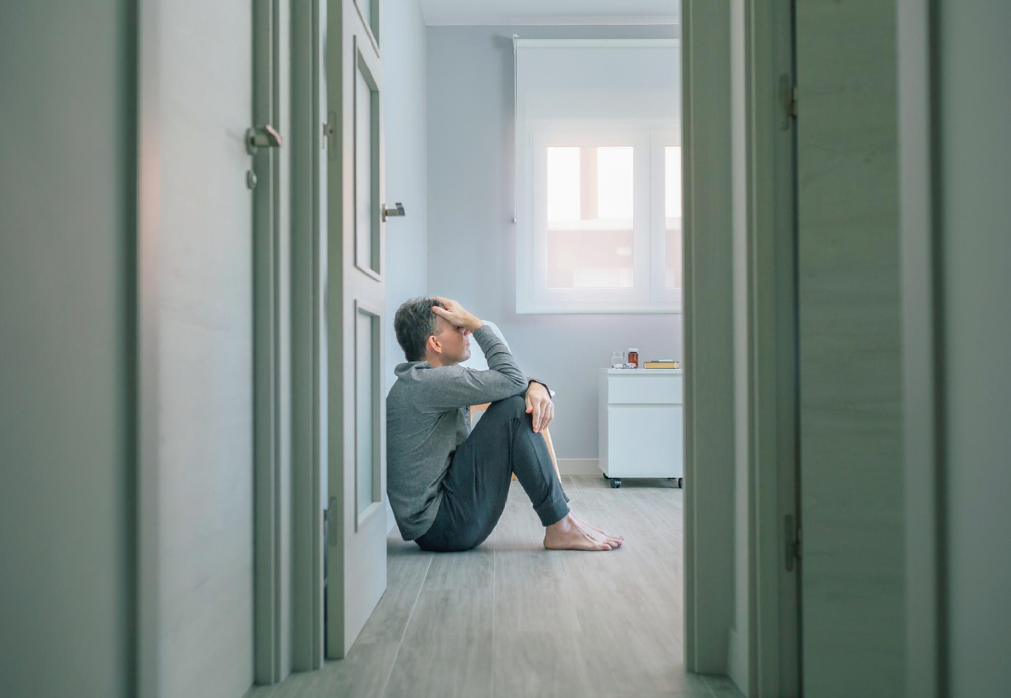 Desperate man with suicidal thoughts holding his head with hand sitting on the floor