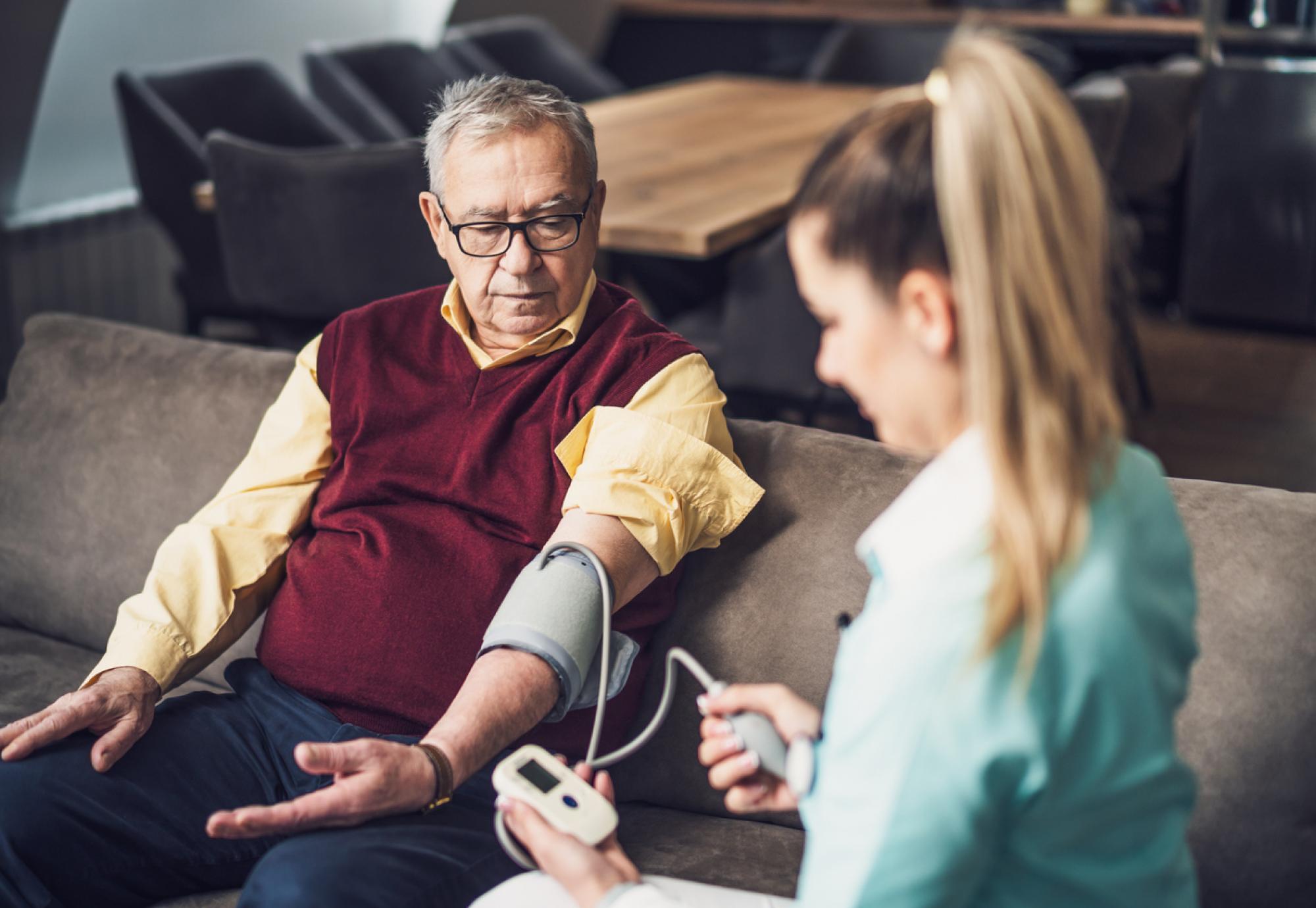 Home doctor is measuring blood pressure of old man at his home