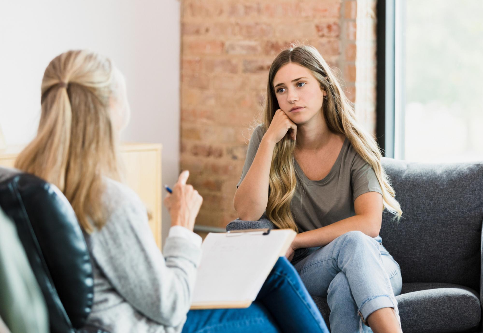 Teen girl listens to advice from unrecognizable female therapist