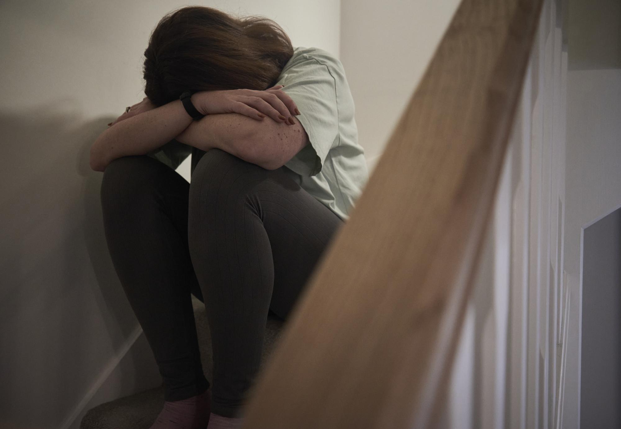 A woman suffering from depression or domestic abuse sat on the stairs of her home hiding her face.