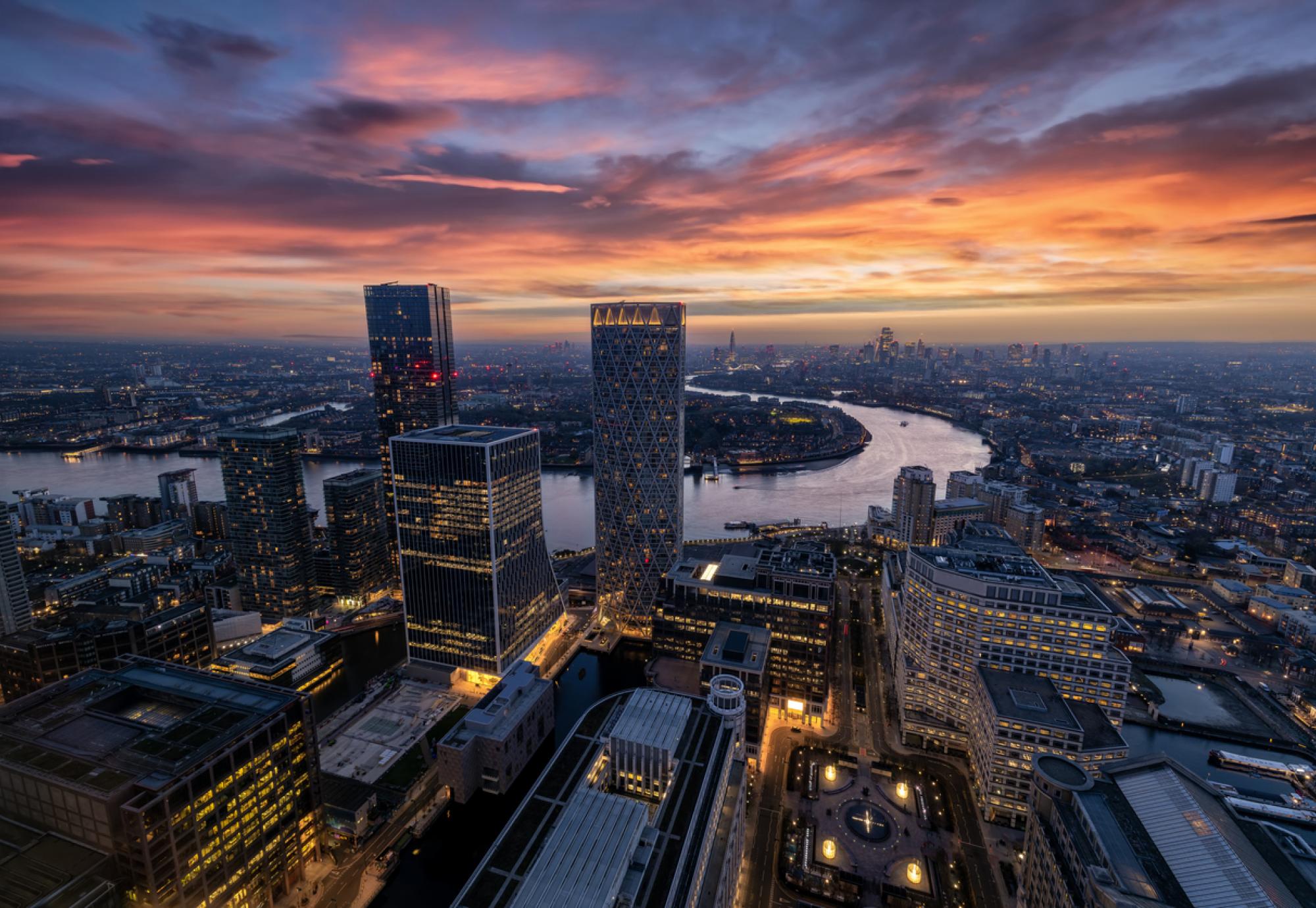 Panoramic view through the modern skyscrapers of Canary Wharf of the illuminated London skyline and Thames river during dusk time, England