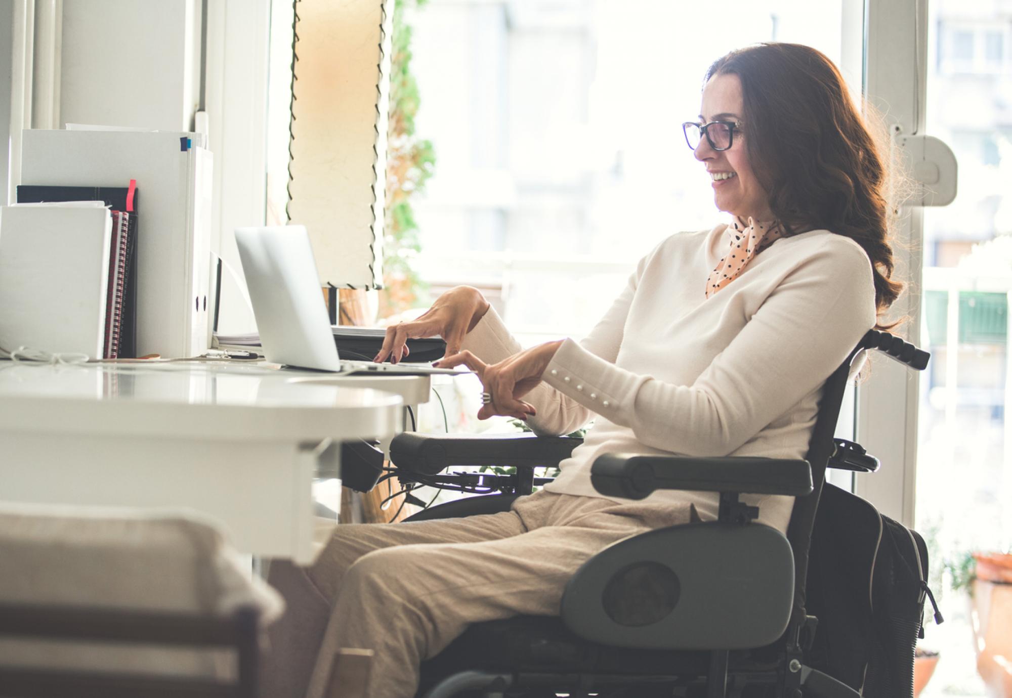 Side view of a happy woman with physical disability working on a laptop