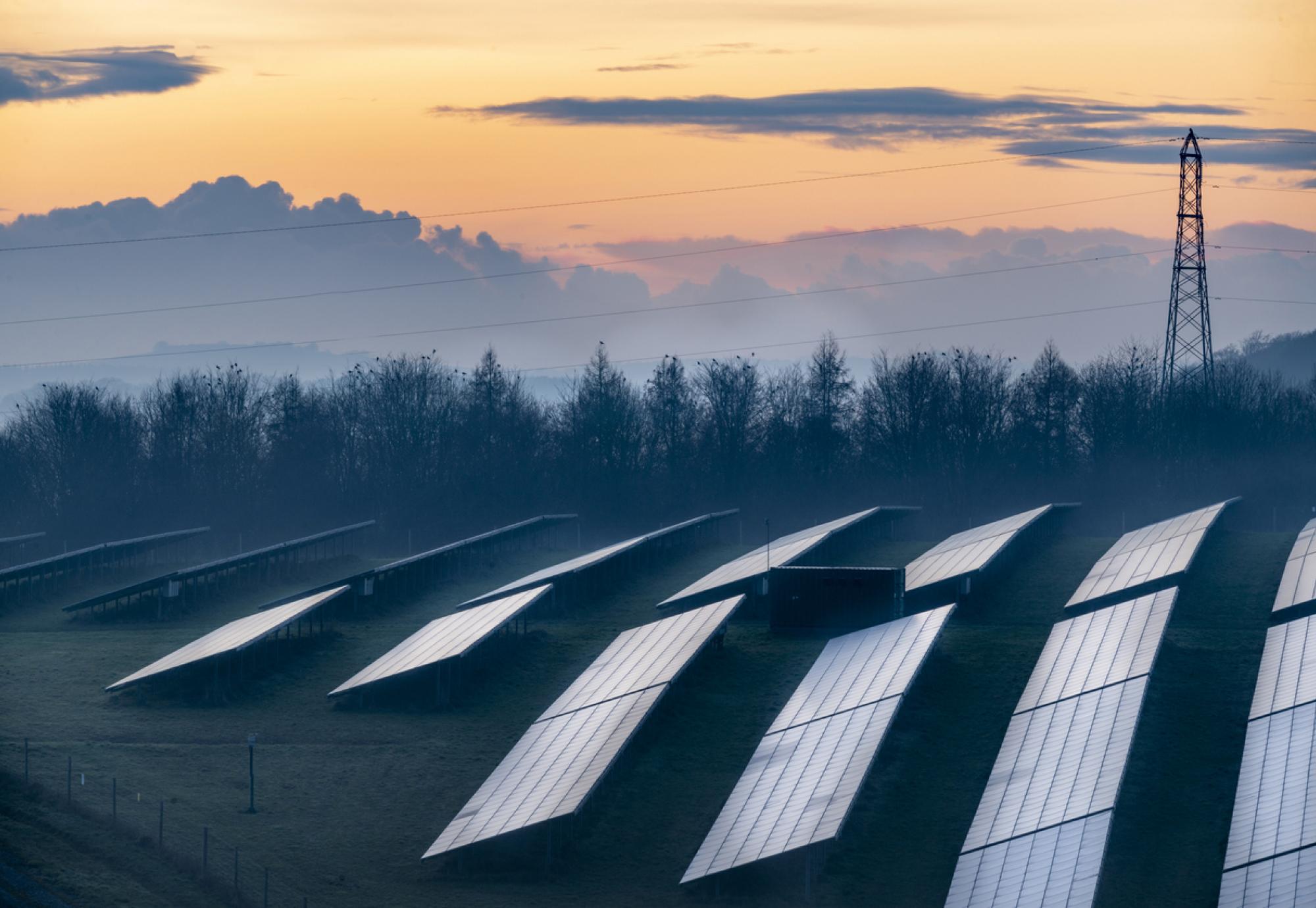 Solar energy park and conventional electricity pylon at sunset, Hampshire, England