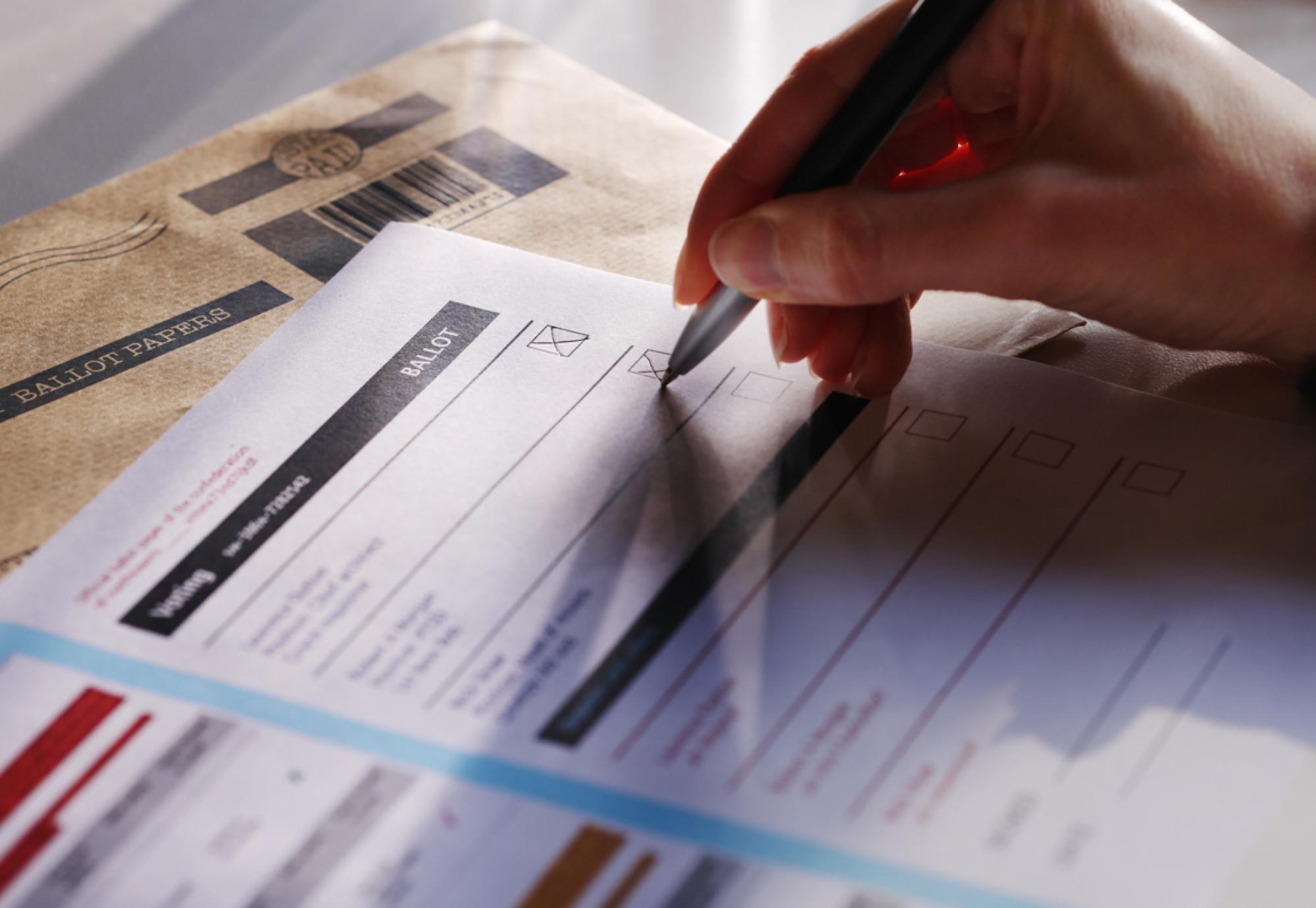 a woman’s hand filling in a postal ballot  voting form.