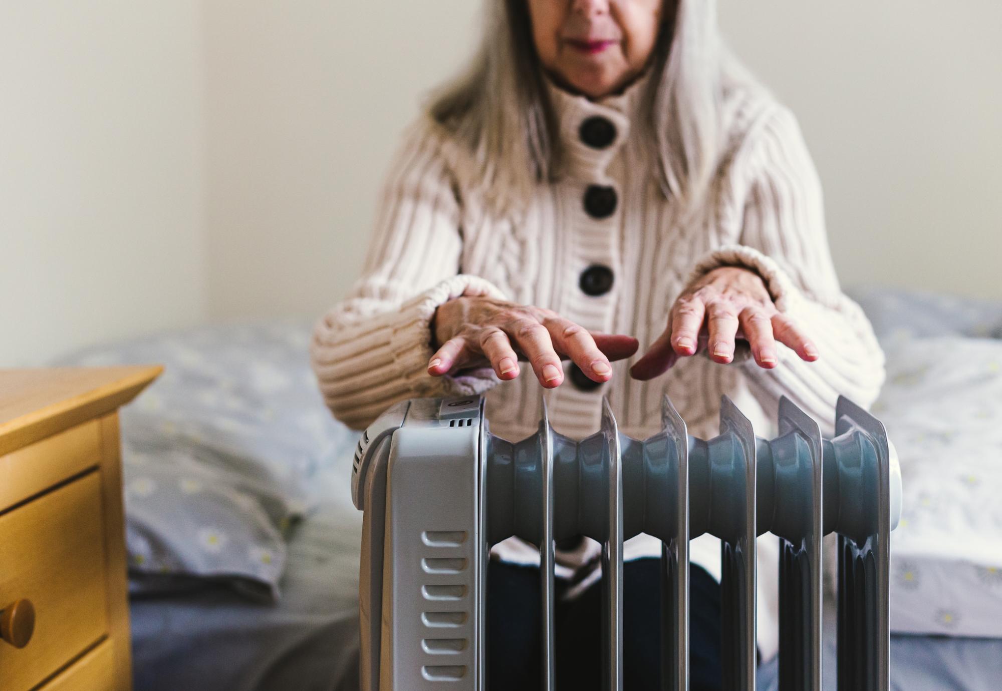 A pensioner sits in her cold home, next to a space heater
