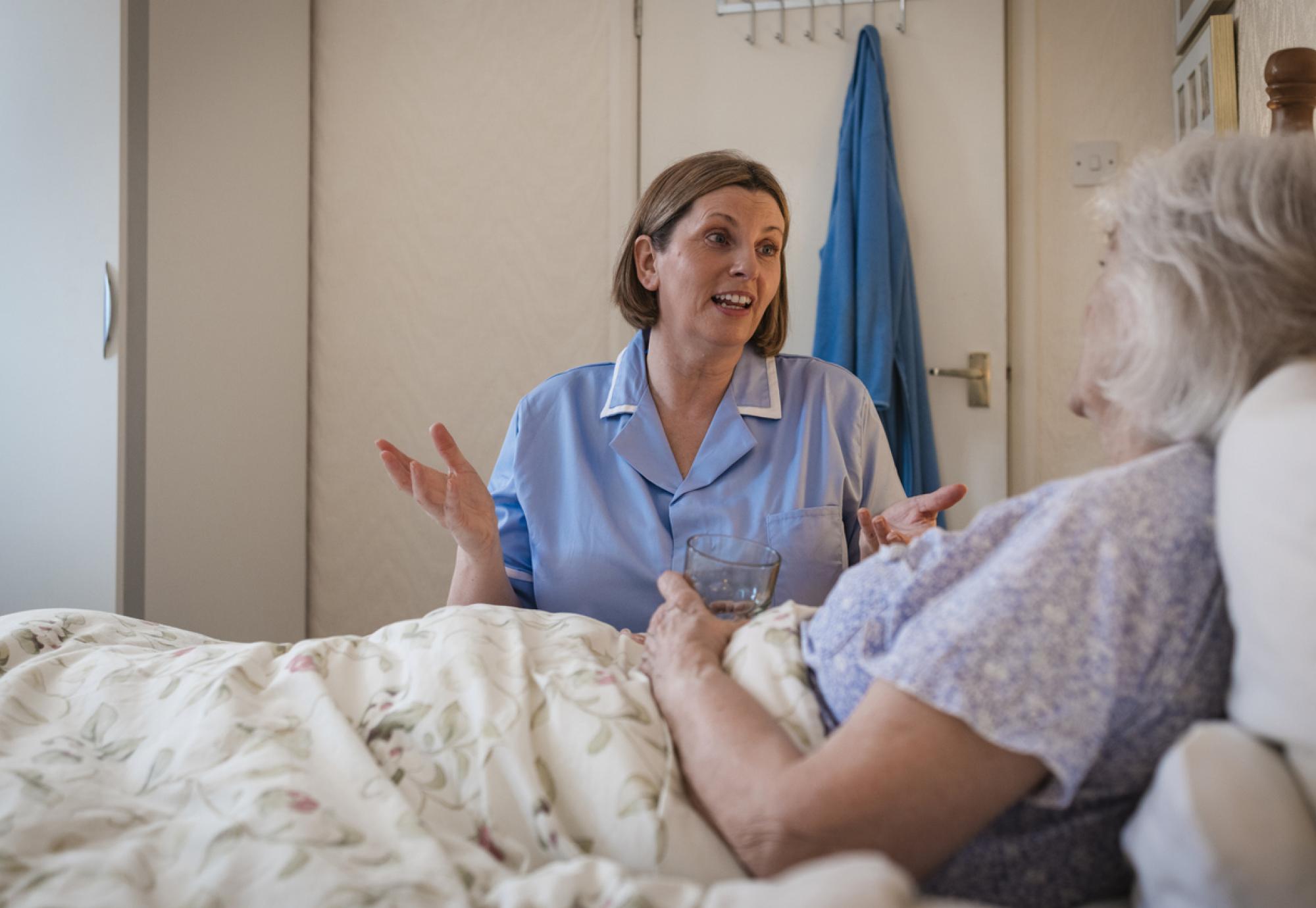 Senior woman lying in bed being helped by a home carer