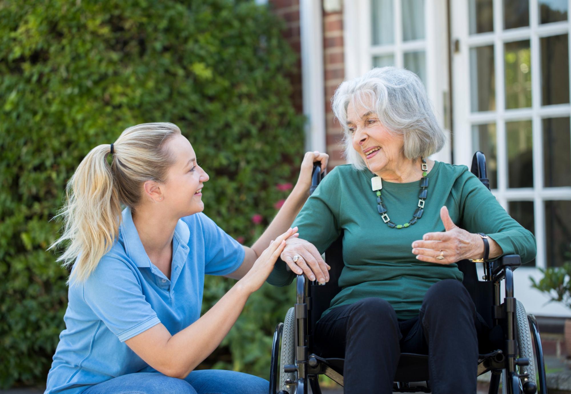 Carer supporting an elderly woman in a wheelchair