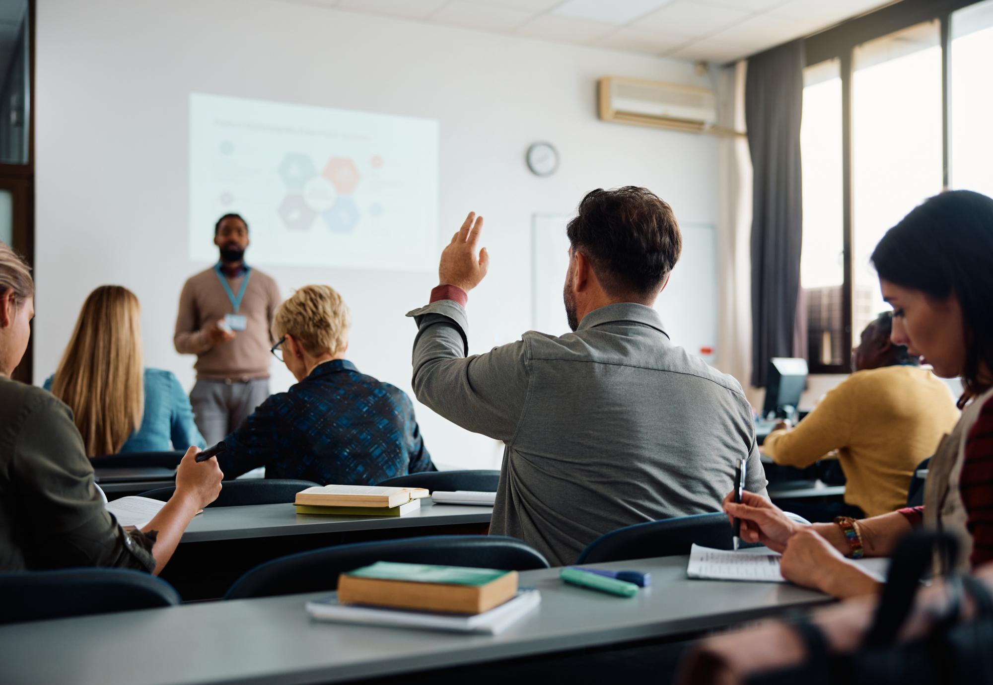 Rear view of man raising arm to ask a question during a presentation