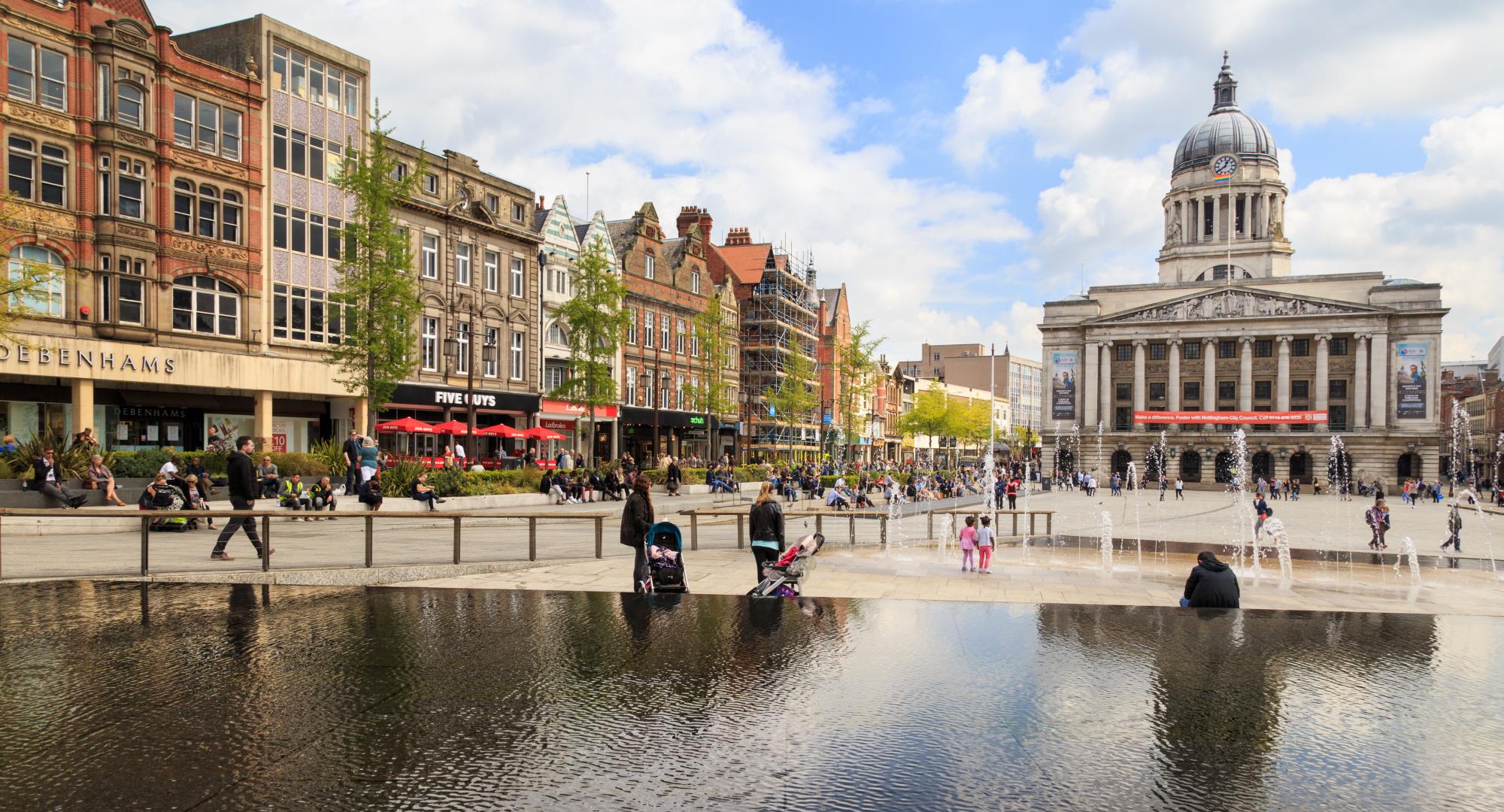 Various people sitting, walking, visiting in the main Market Square, Nottingham Council House building behind.