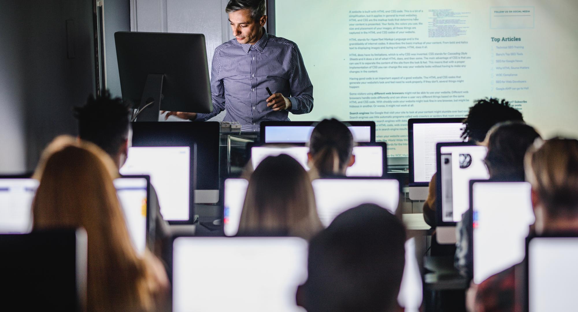 Male teacher giving a lecture from desktop PC during a class at computer lab.