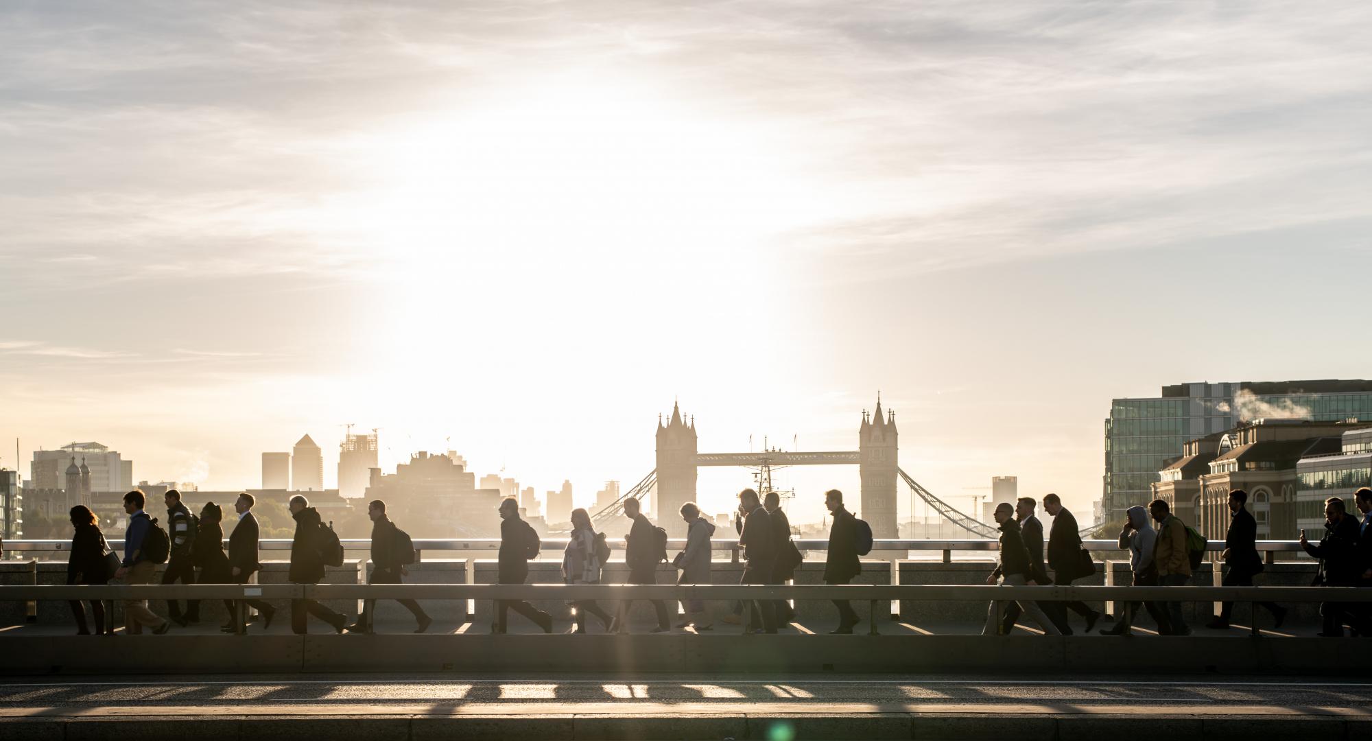 Morning rush hour across London Bridge at dawn. Bright sunlight and Tower Bridge in the background