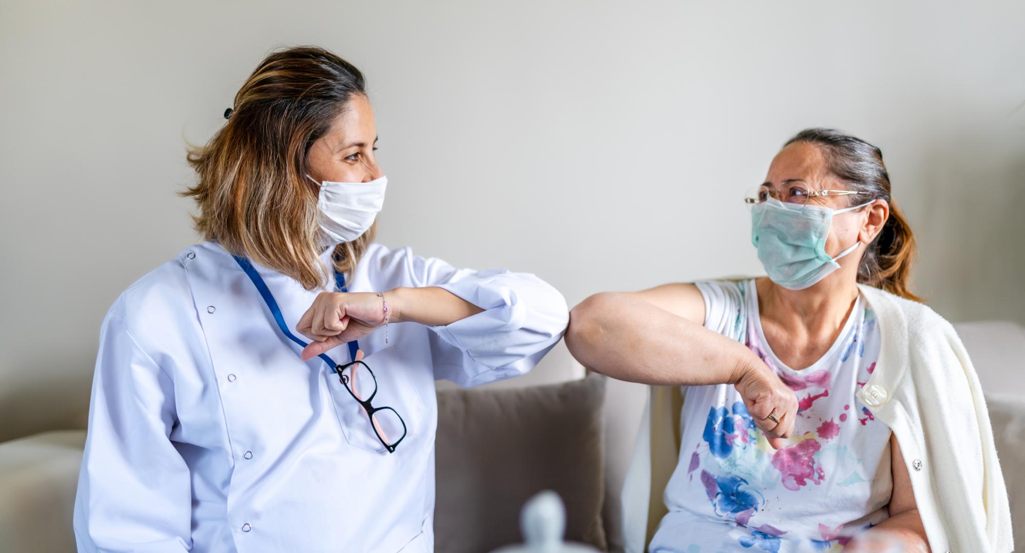 Nurse and patient bumping elbows in a care home, with face coverings on.