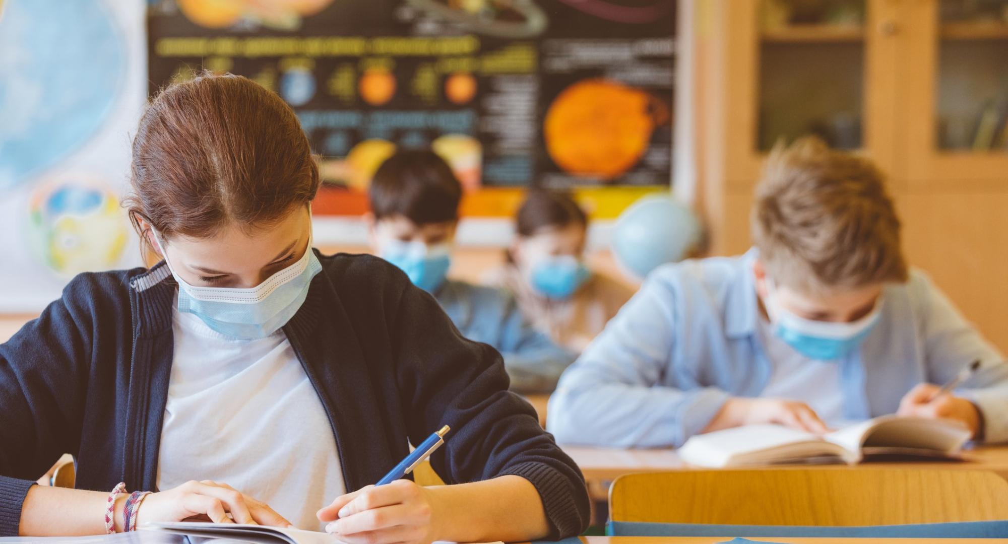 Children working in a classroom, socially distanced with face masks on.