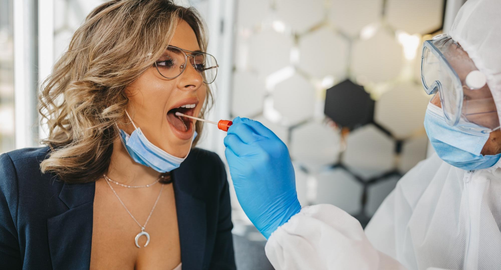 Woman in glasses receives Covid test from man wearing PPE.