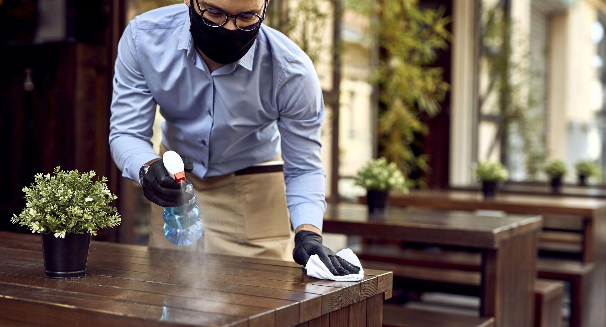 Waiter cleans table with antibacterial spray and wipe.