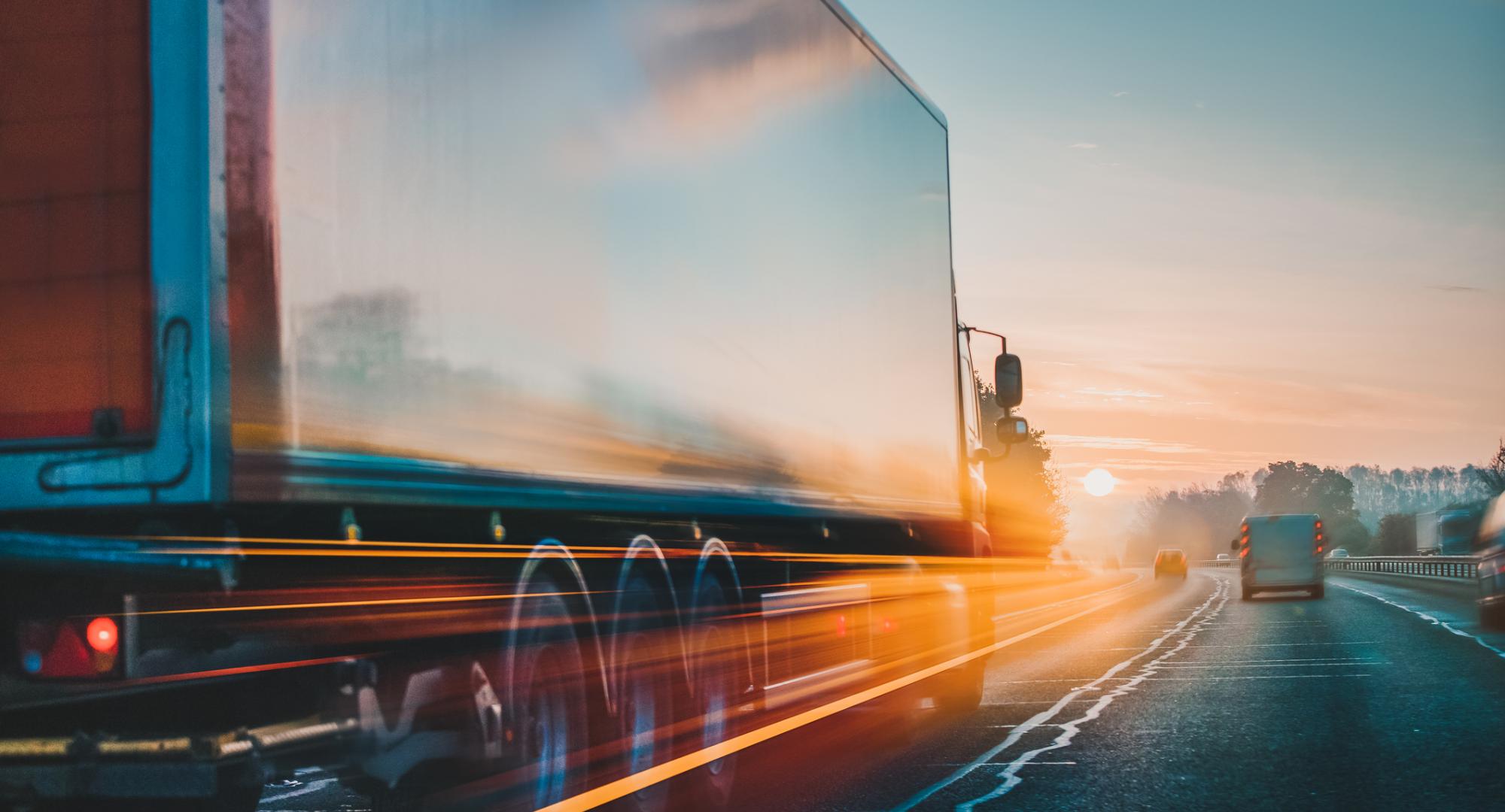 HGV travelling down an A-road, with the sun setting up ahead.