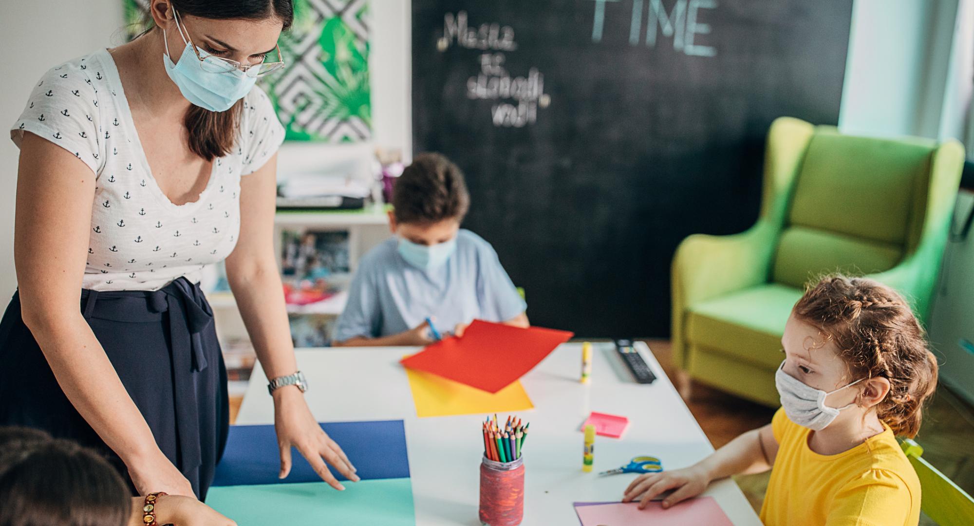Teacher in a face mask teaches small child.