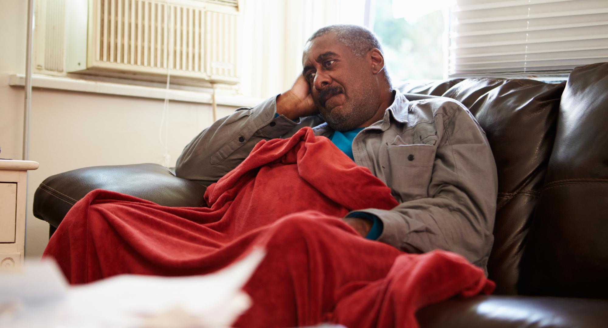 Man is cold in house with blanket around him.
