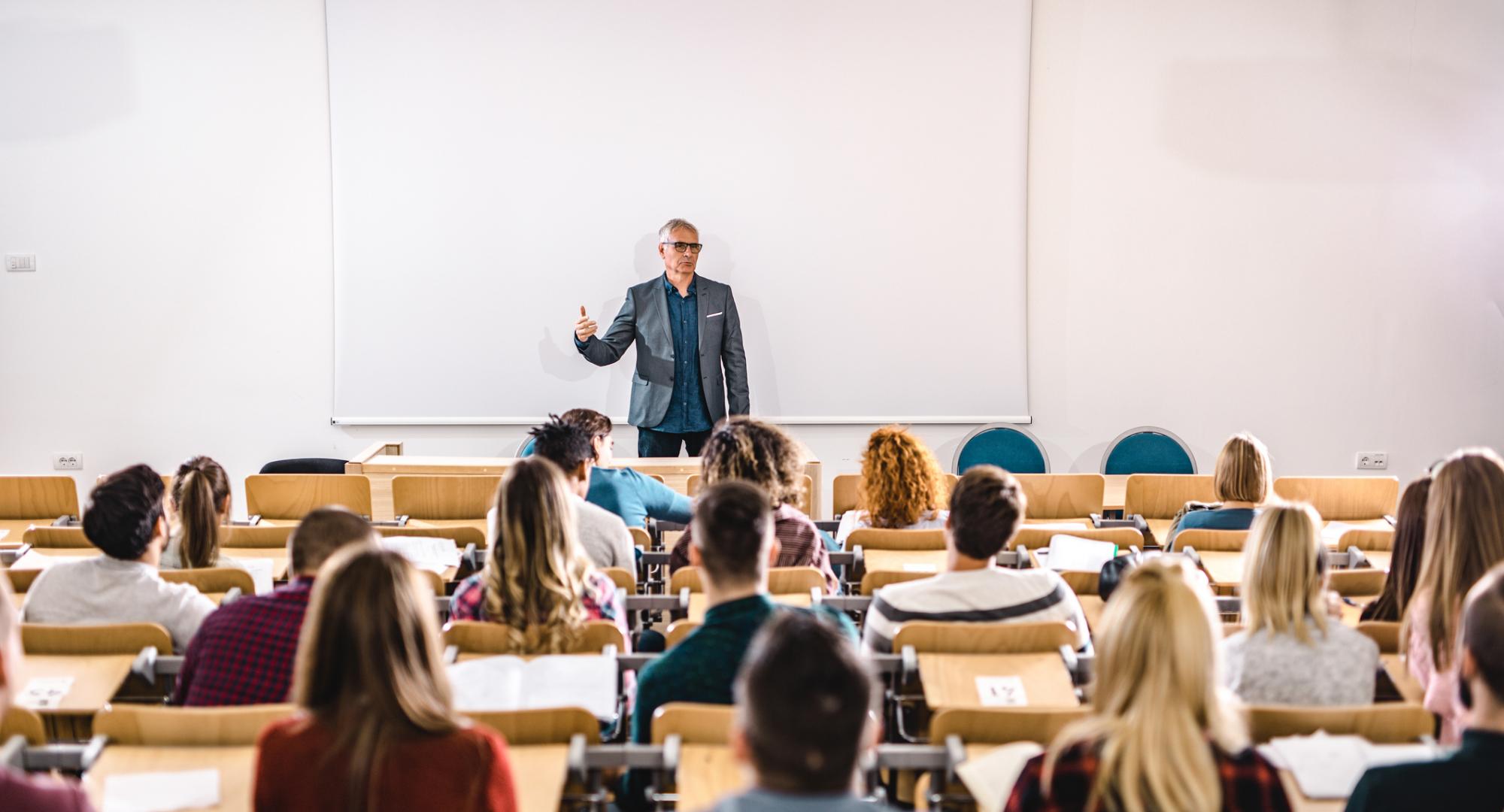 Lecturer stands teaching students in a lecture hall.