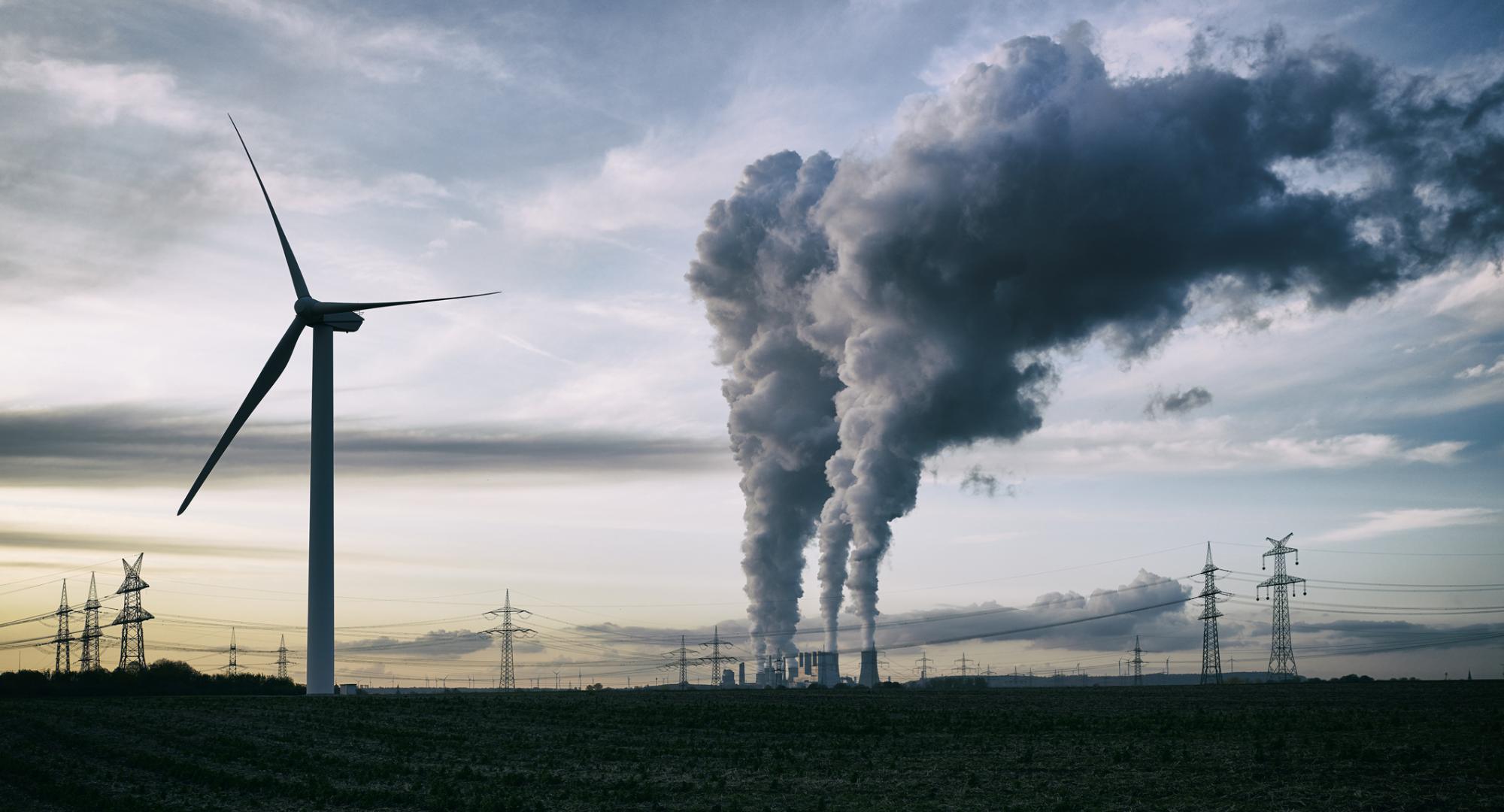 Wind turbine stands in the foreground as coal power station puts steam into atmosphere.