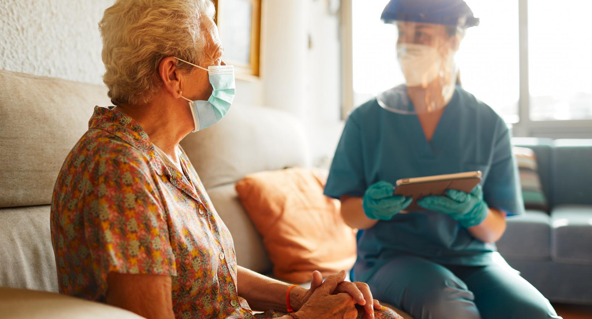 Care home nurse sits with resident in PPE. 