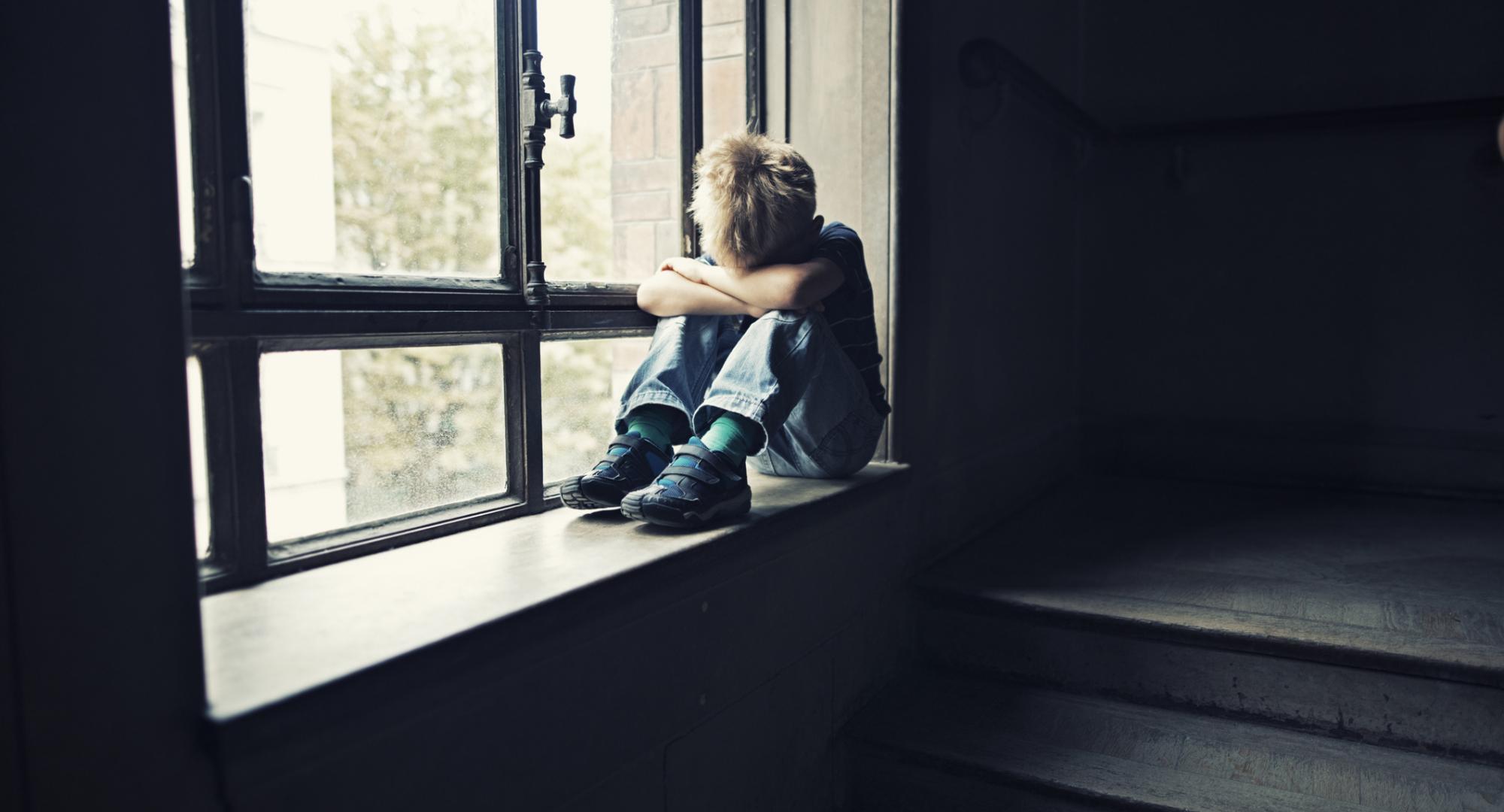 Lonely child sits in window. 