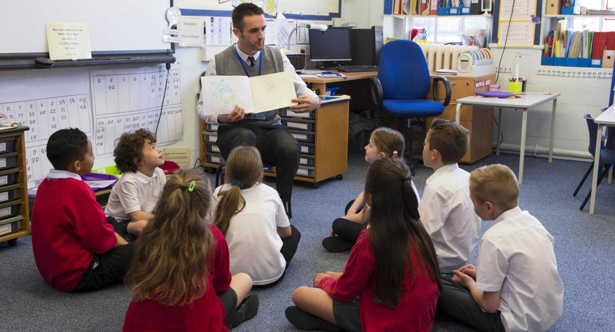 Children sit with teacher as he reads a story.