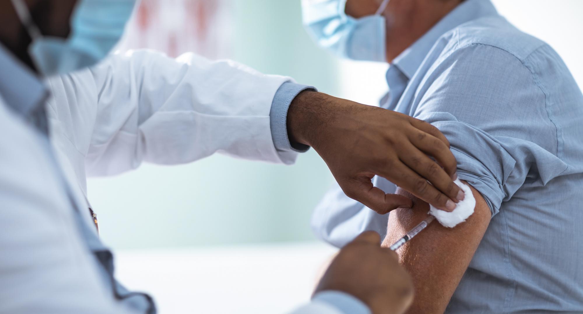 Man receives Covid-19 vaccine from nurse wearing full PPE