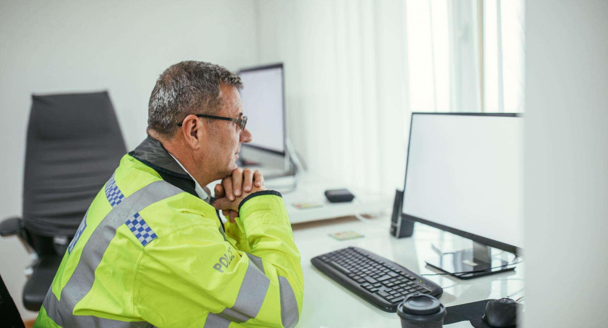 Poliec officer at a desk staring at a computer screen