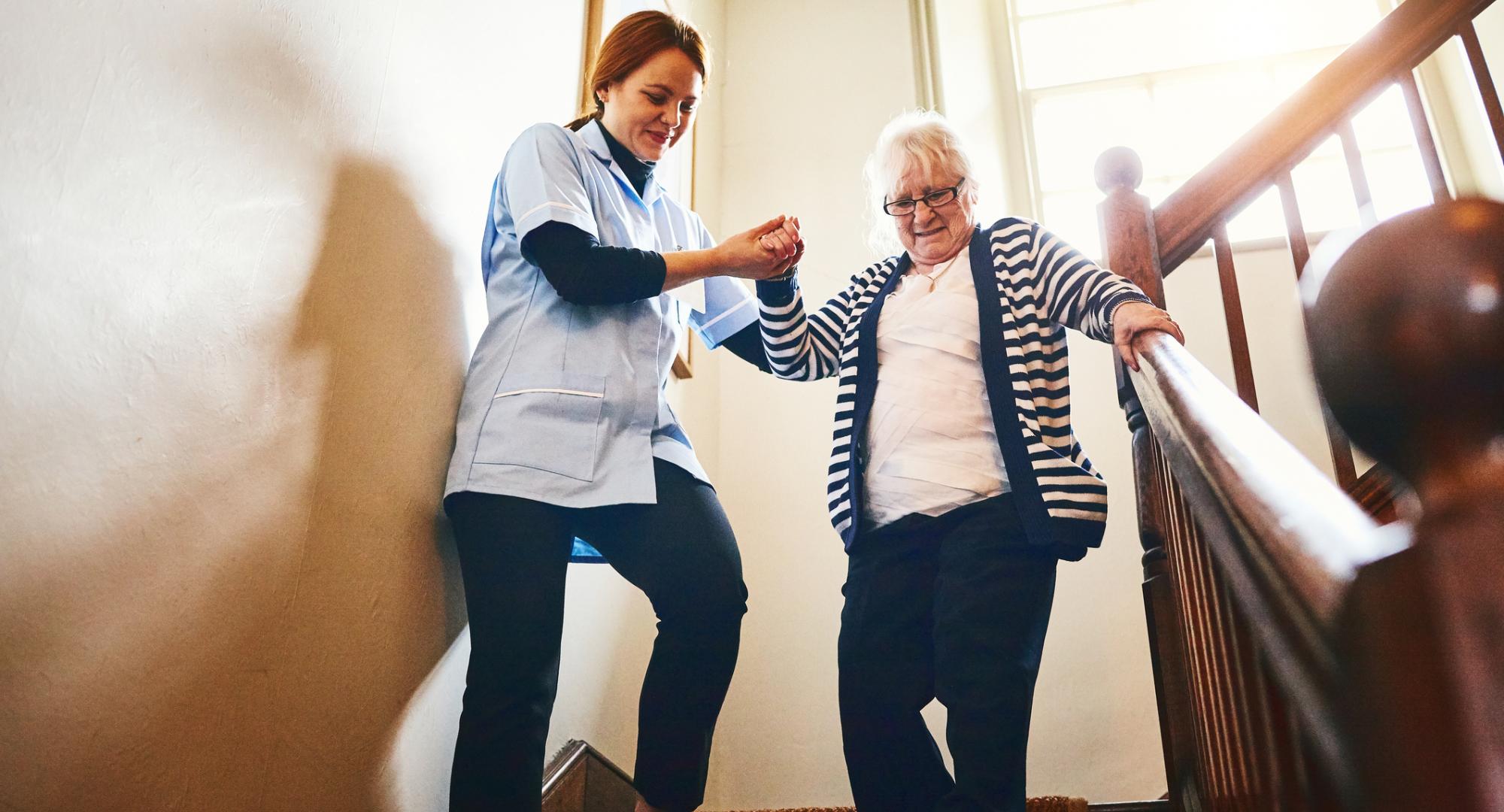 Social care worker helping woman walk down stairs