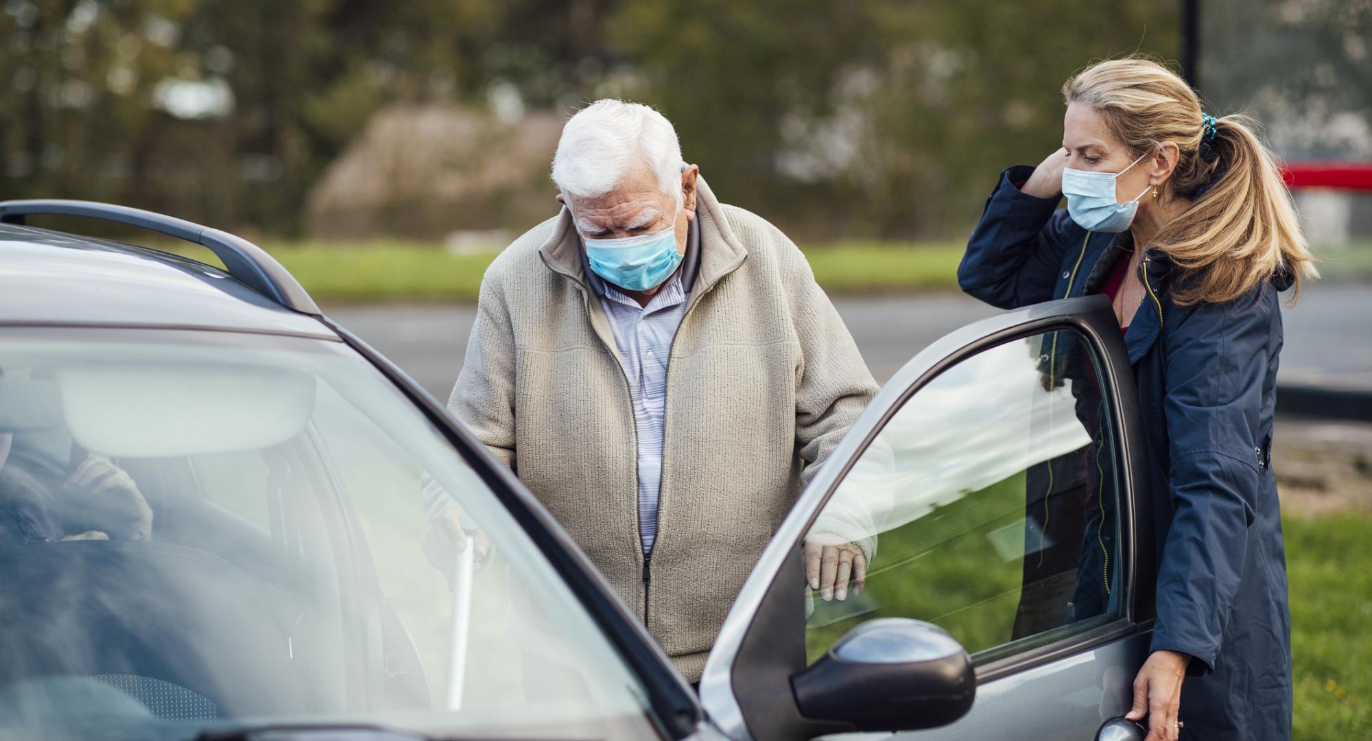 Carer helping elderly man into car