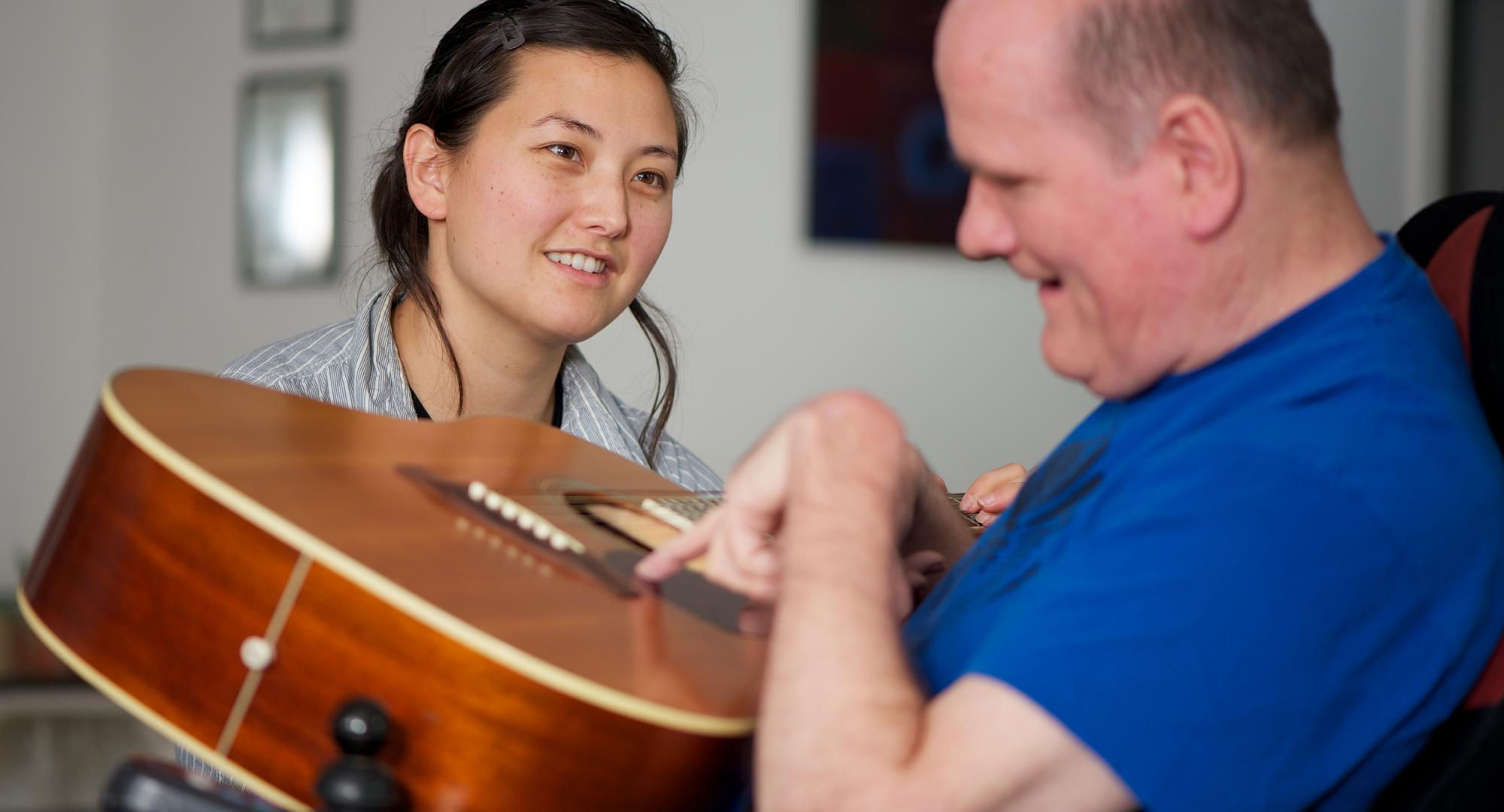 Social care worker sitting with a disabled man as he plays guitar