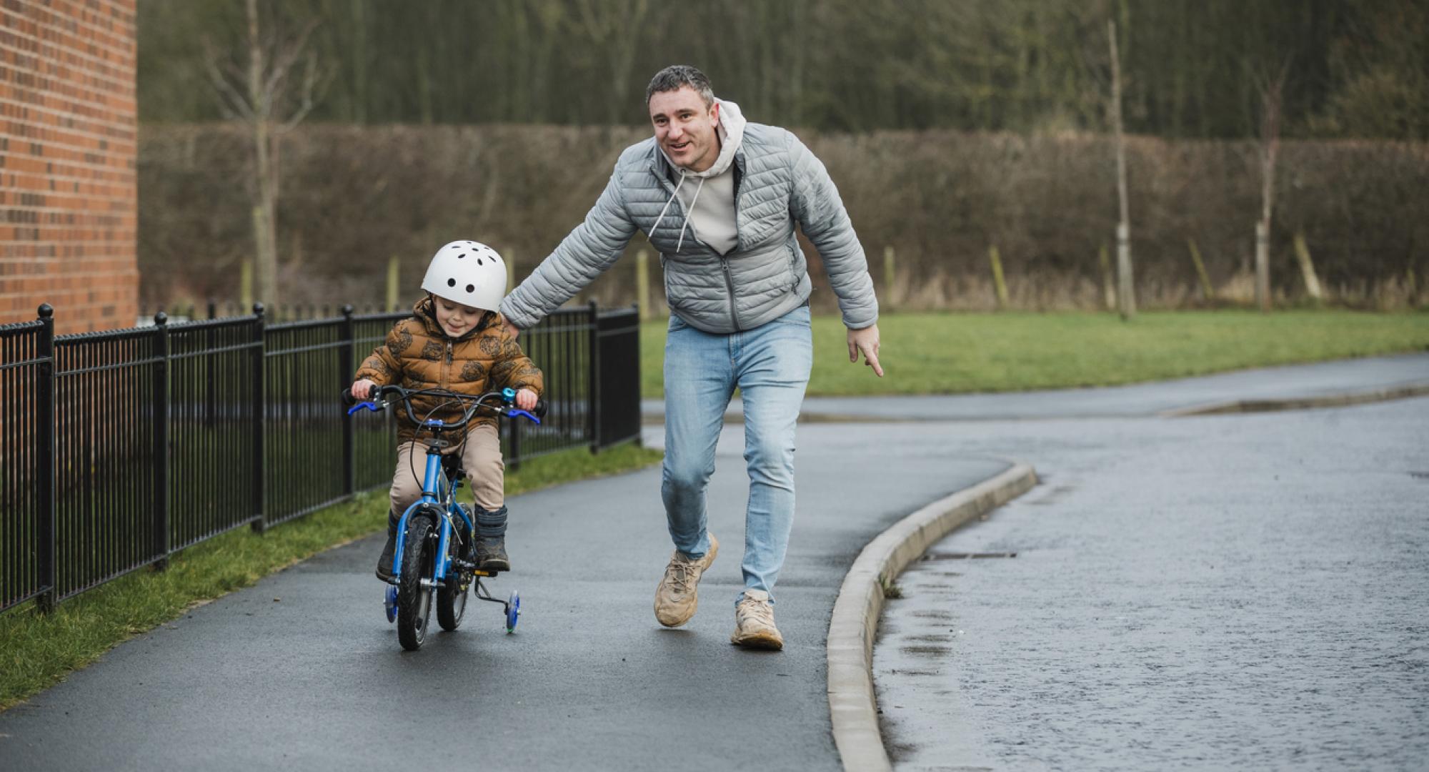 Young boy learning to ride a bike with his dad