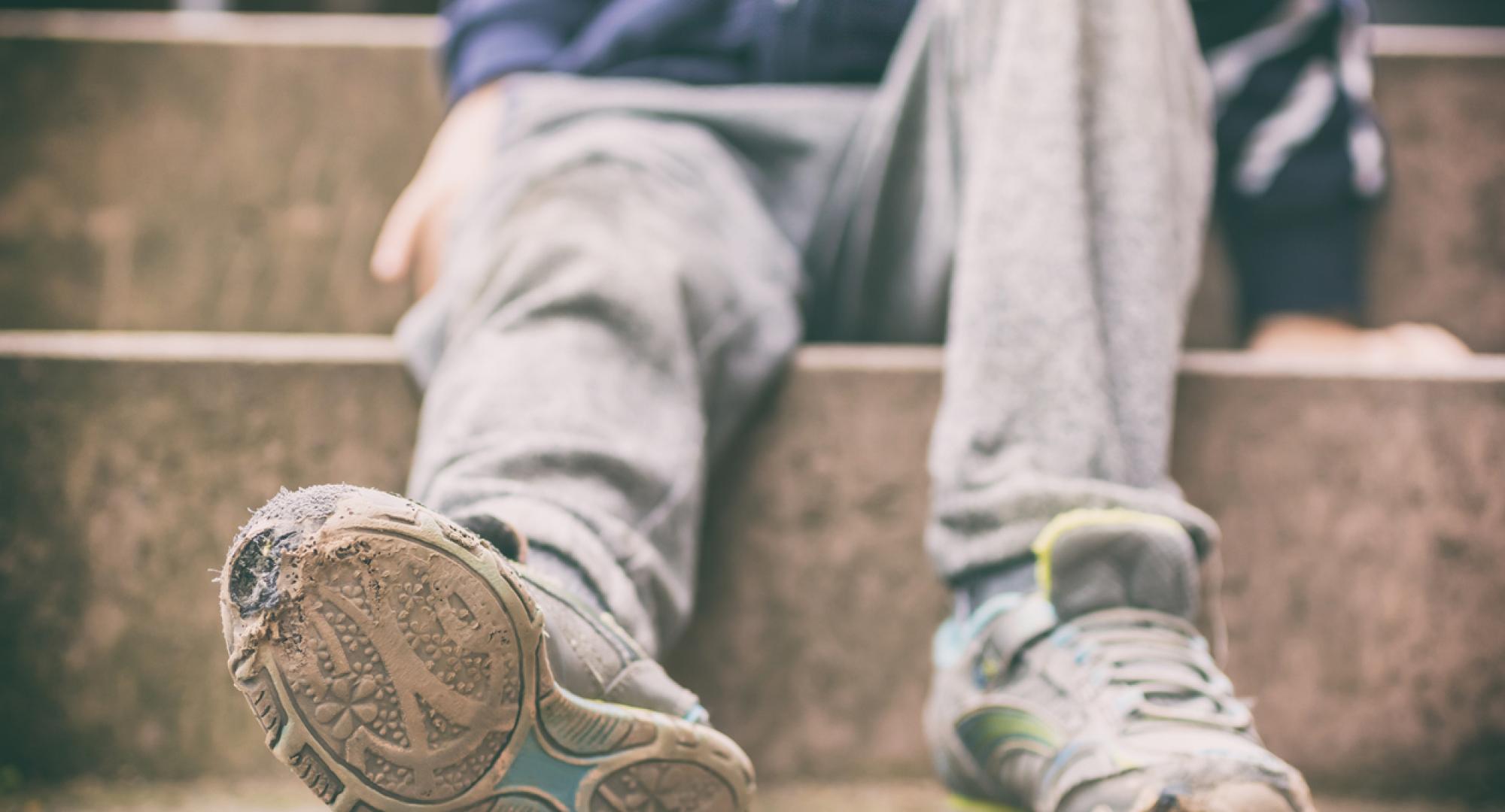 The torn shoes and dirty clothes of a child in poverty