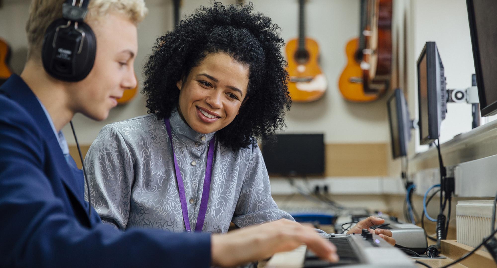 A teacher helping a male student learn to play the keyboard