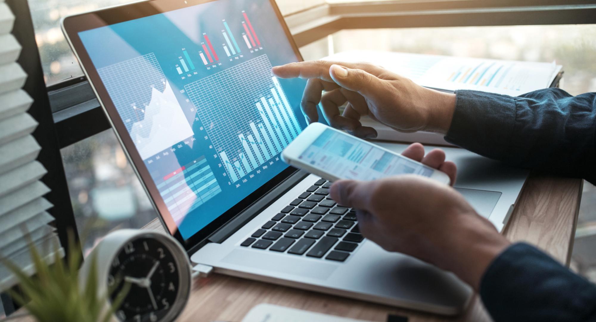 Someone doing business on a laptop and a mobile phone, with a graph on the screen