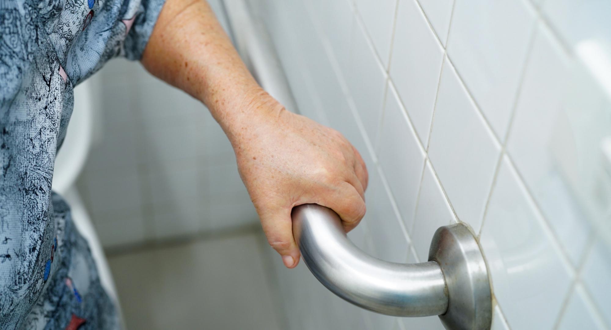 A disabled elderly woman using a handrail to steady herself in the toilet