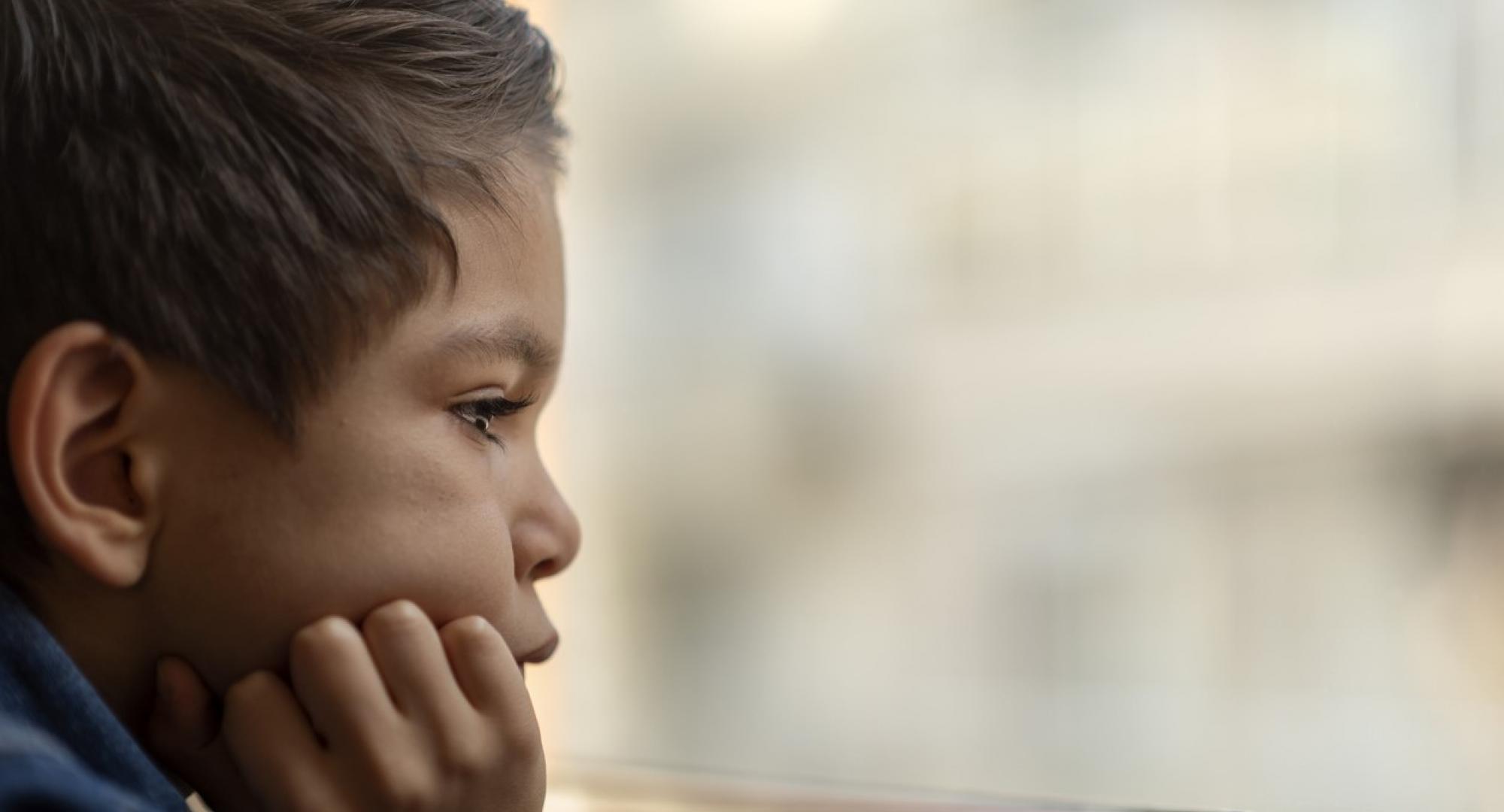 A sad child looks out of a window