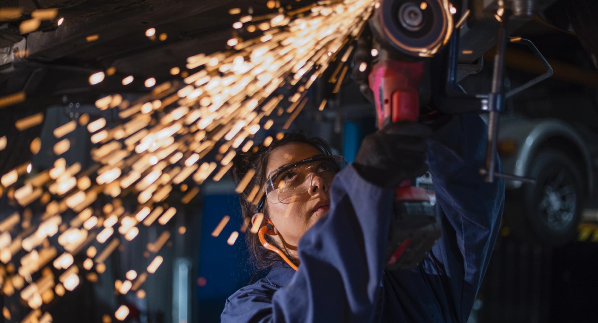 Low angle close up view of a female mechanic using an electric grinder tool on the base of a car while working at a car garage