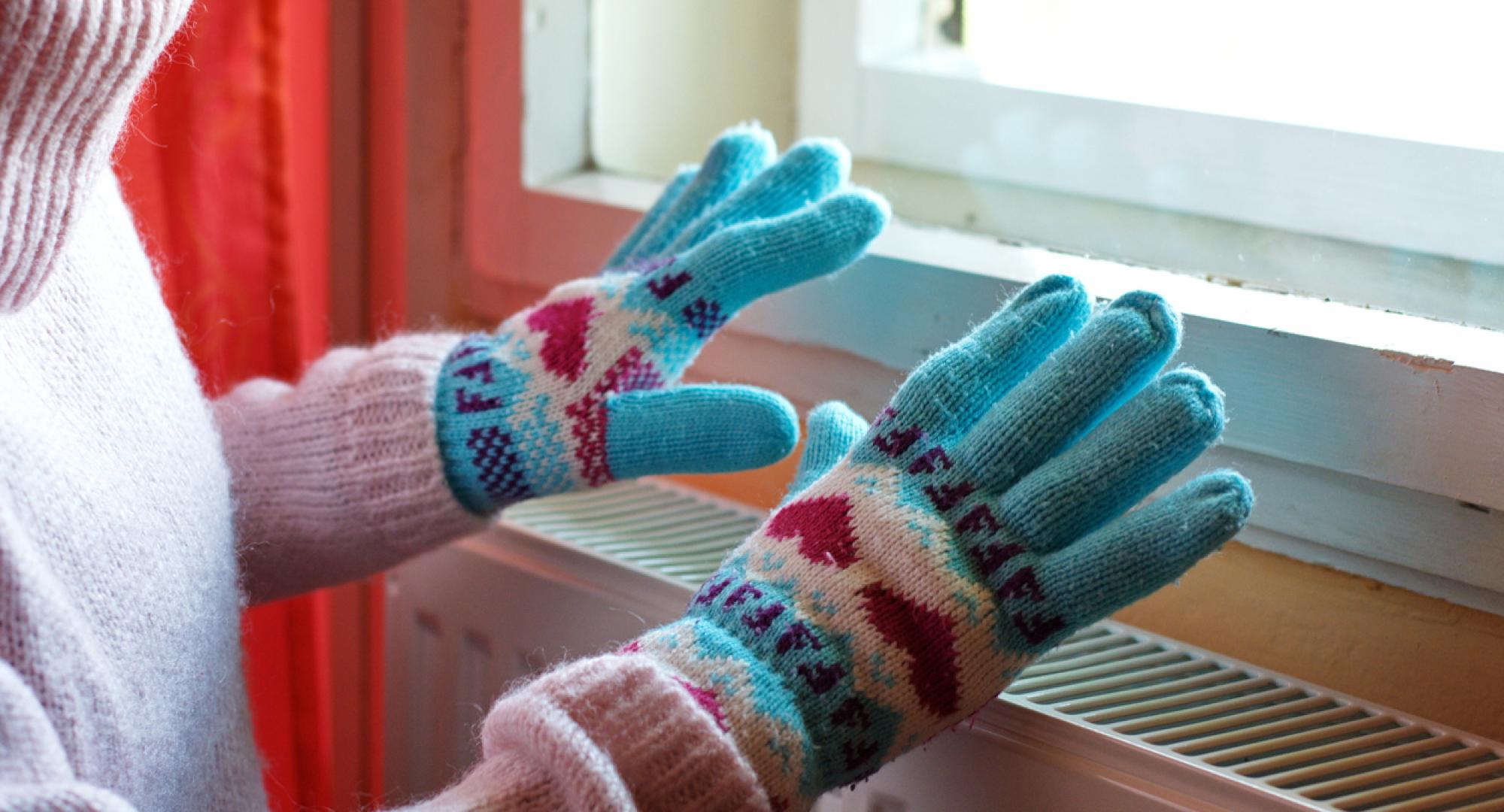Woman heating gloved hands on raditator