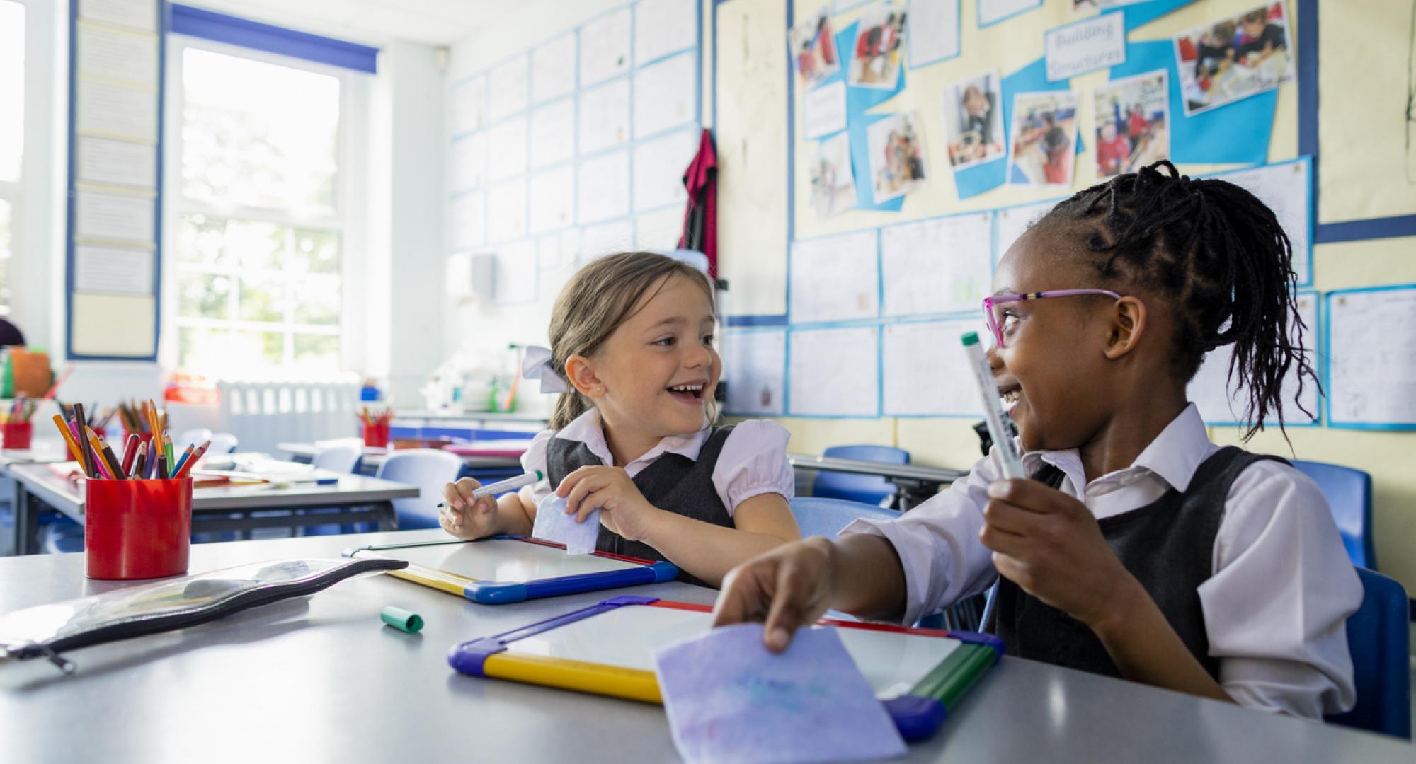 Primary school students sitting in a classroom writing on a mini whiteboards 